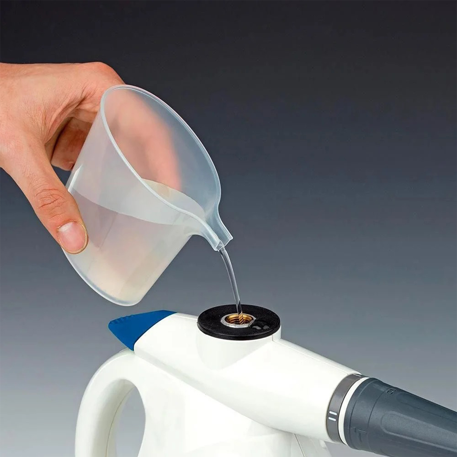 Una mano versa l'acqua da un misurino trasparente in un pulitore a vapore bianco e blu.