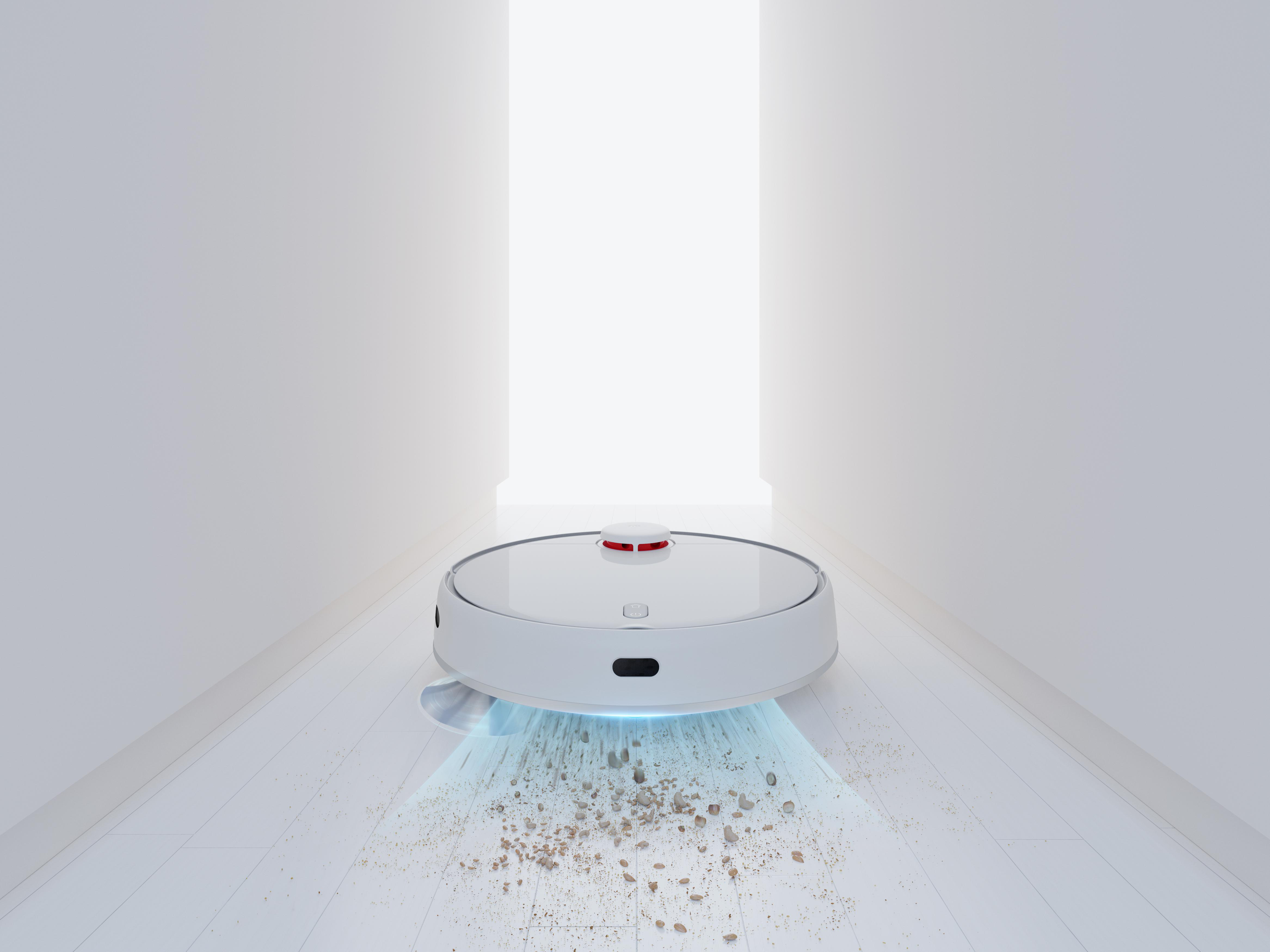 Weißer Roboter-Staubsauger. Reinigt einen Holzboden. Schmutz davor. Licht kommt aus einem Türrahmen.