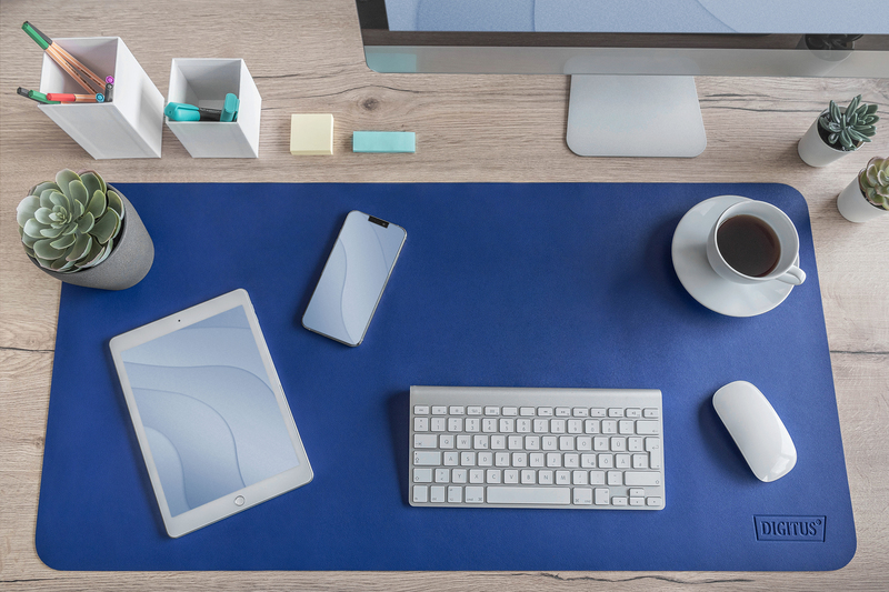 Schreibtisch mit blauer Matte. Tablet, Telefon, Tastatur, Kaffee und Pflanzen sichtbar.