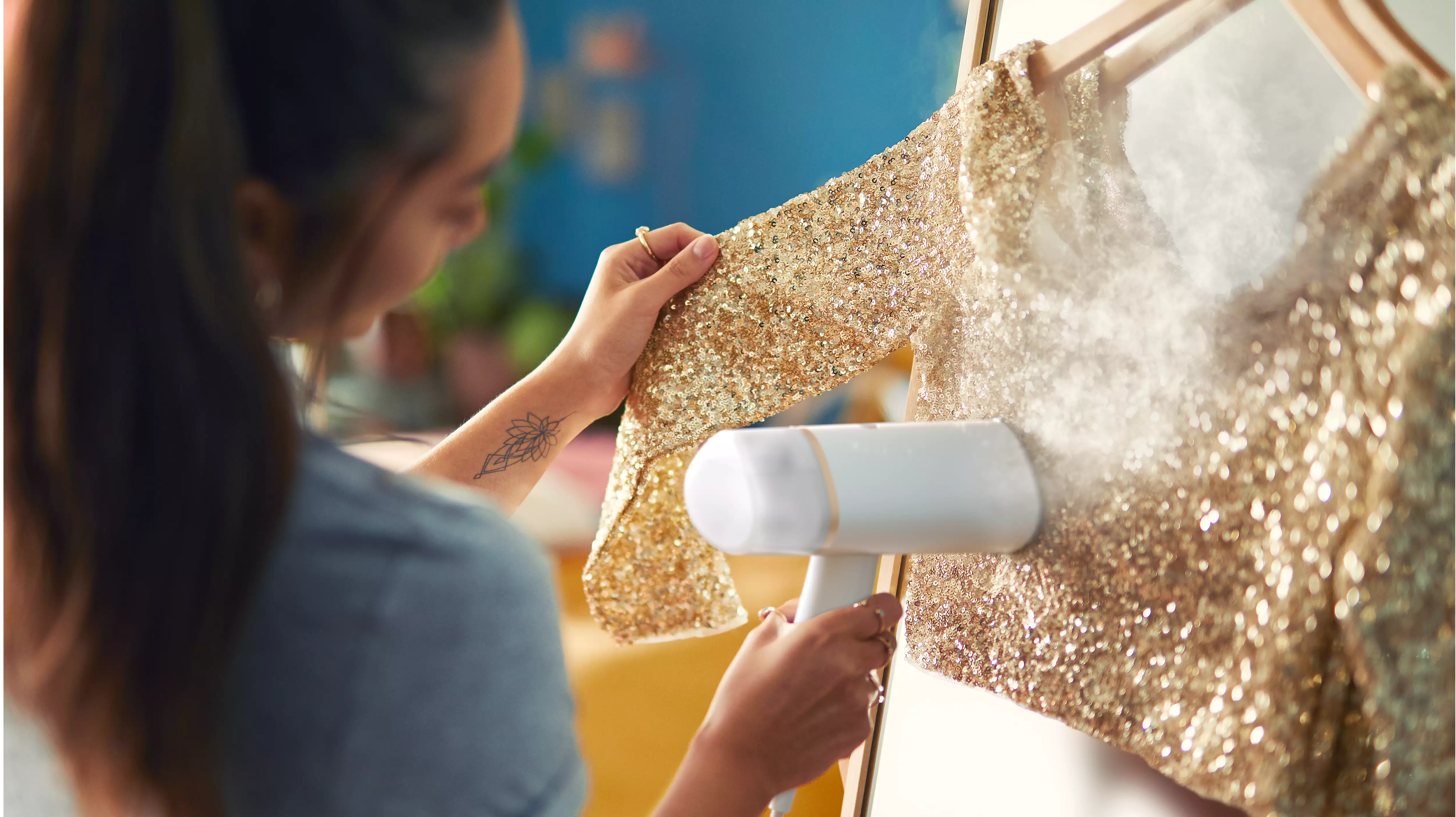 Femme repassant une robe dorée à paillettes sur un cintre avec un défroisseur à main.