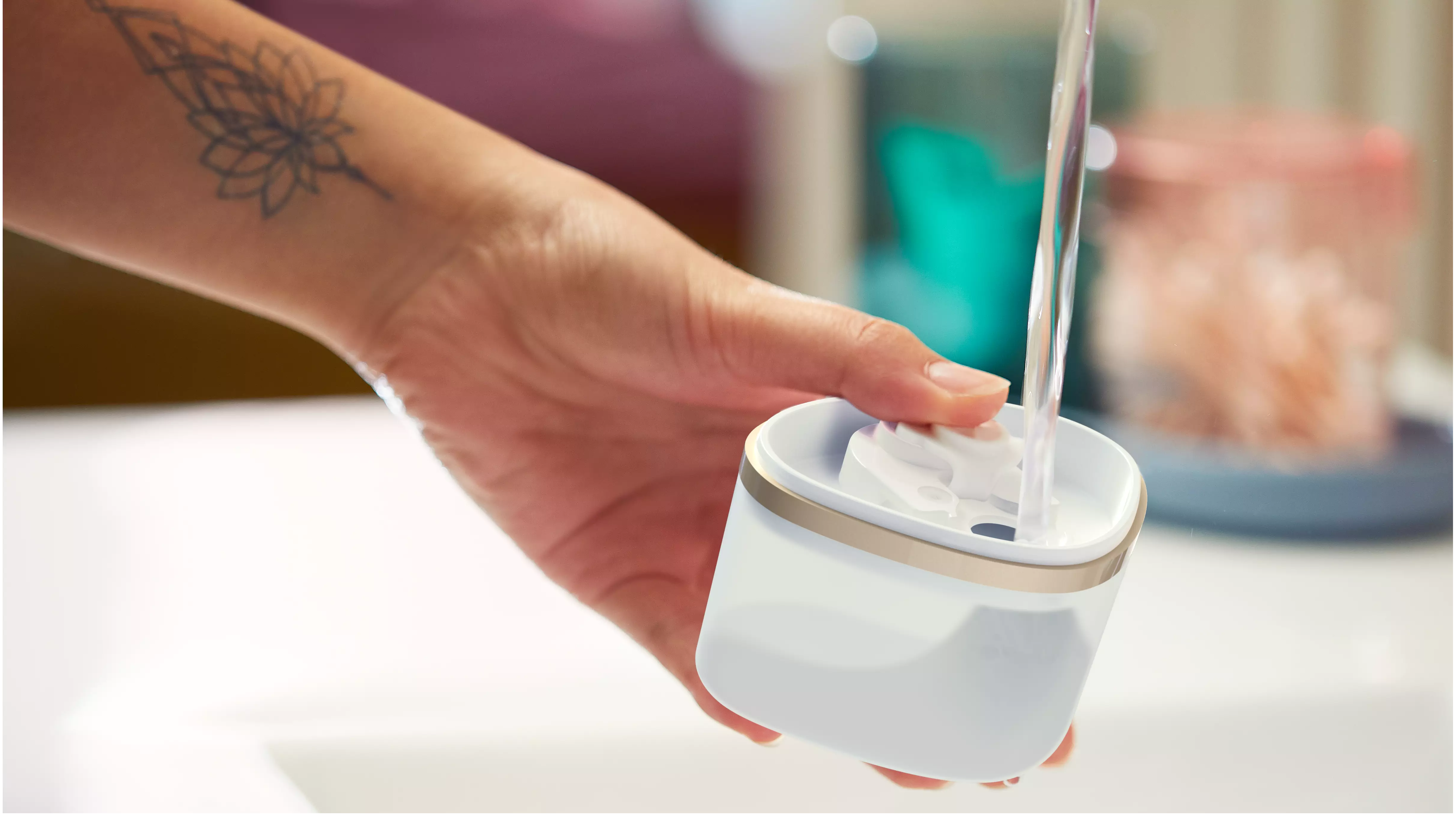 Une main verse de l'eau dans un récipient blanc. Un tatouage est visible sur le bras.