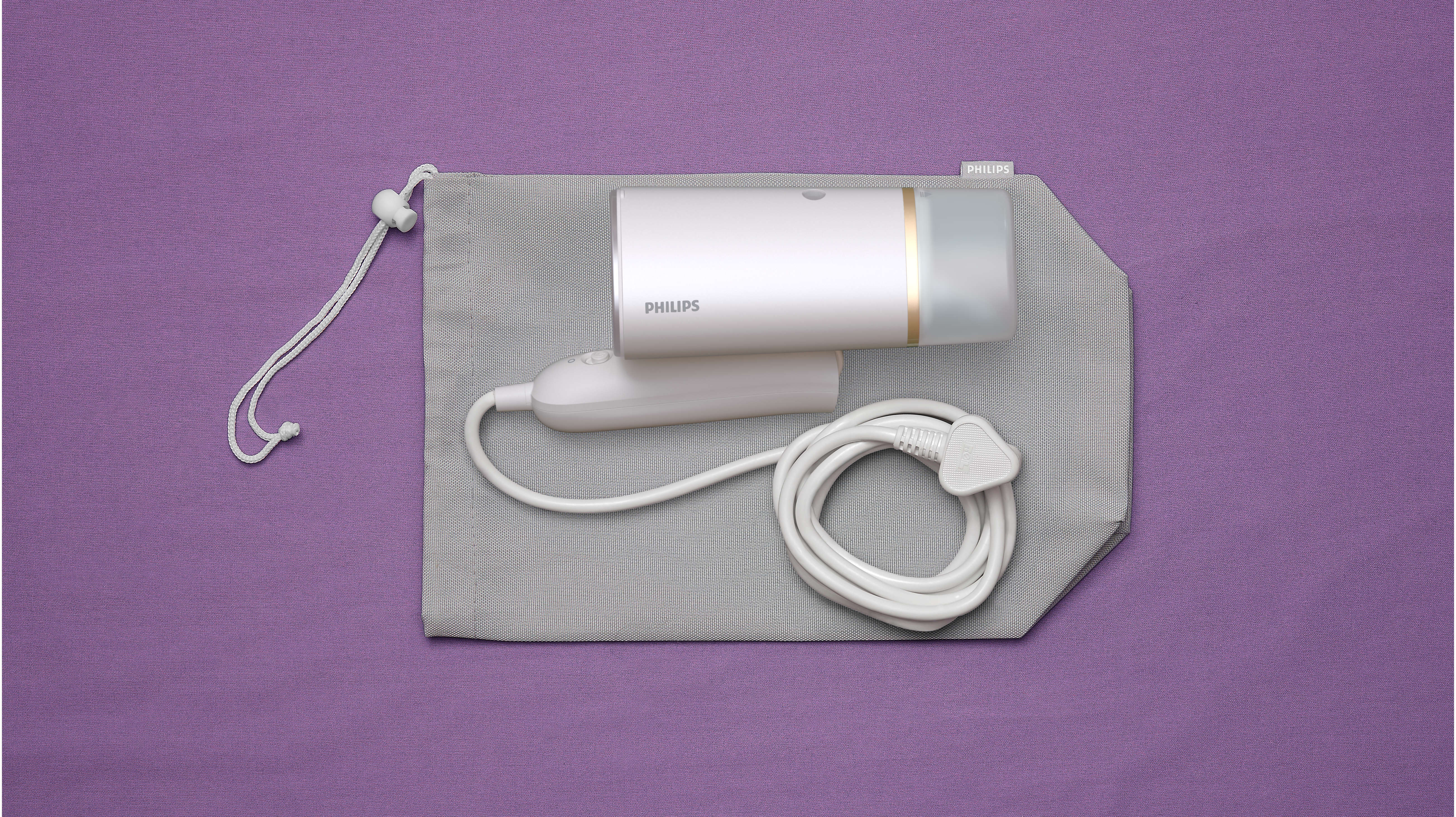 Un défroisseur Philips blanc est dans une pochette grise sur une surface violette. Le défroisseur a un cordon blanc et une prise.