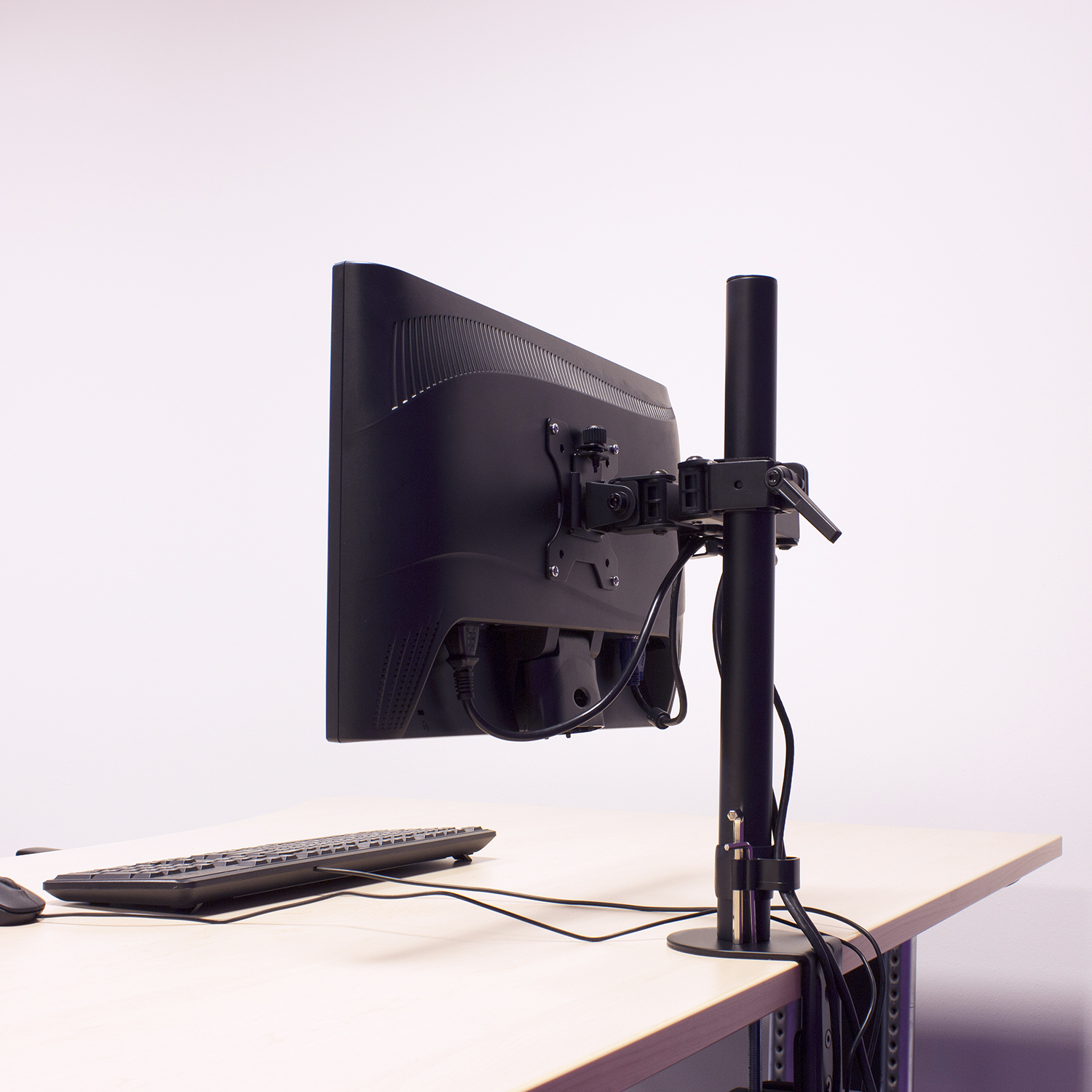 Monitor mounted on a black stand, desk and keyboard in the foreground.