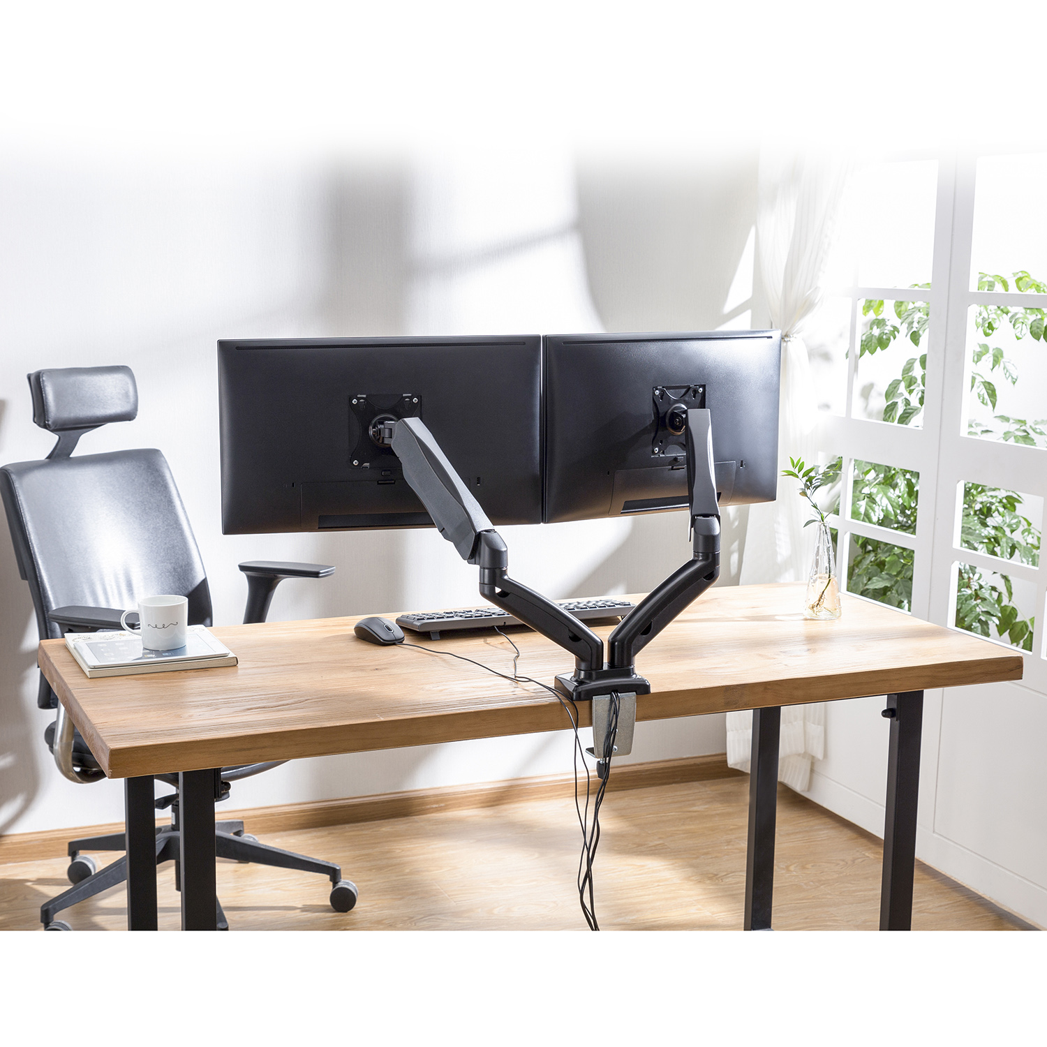 A desk with two monitors mounted on arms. A keyboard and mouse are on the desk.