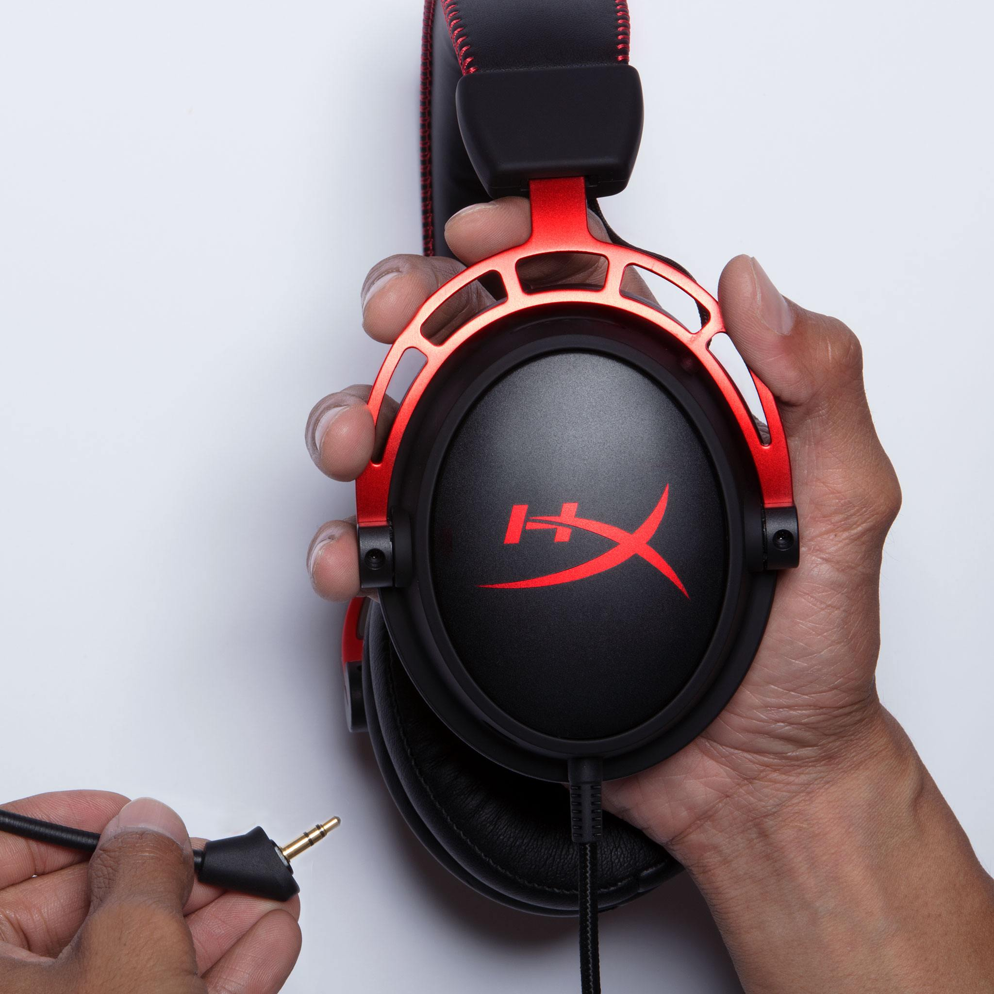 Casque audio, rouge et noir, tenu par des mains, câble et prise jack visibles.