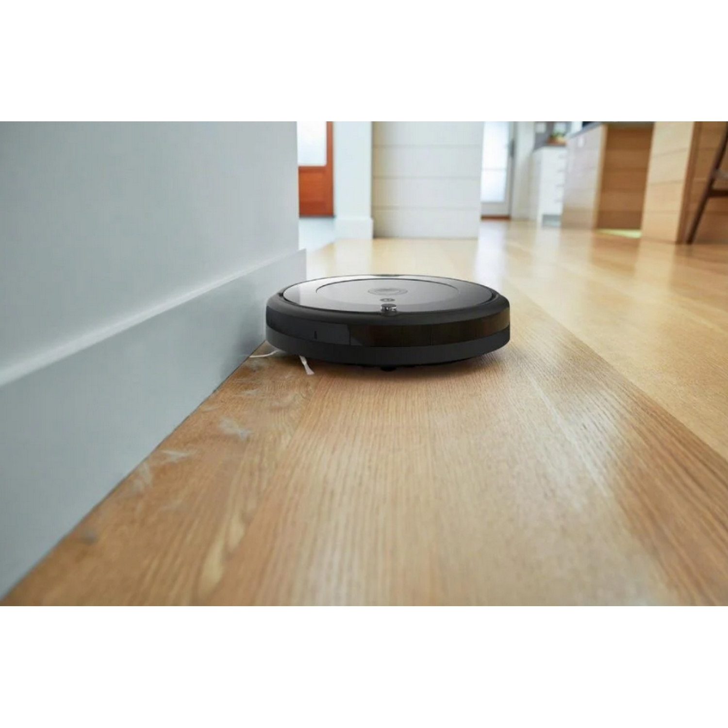 Aspiradora robot negra en suelo de madera, cerca de una pared.