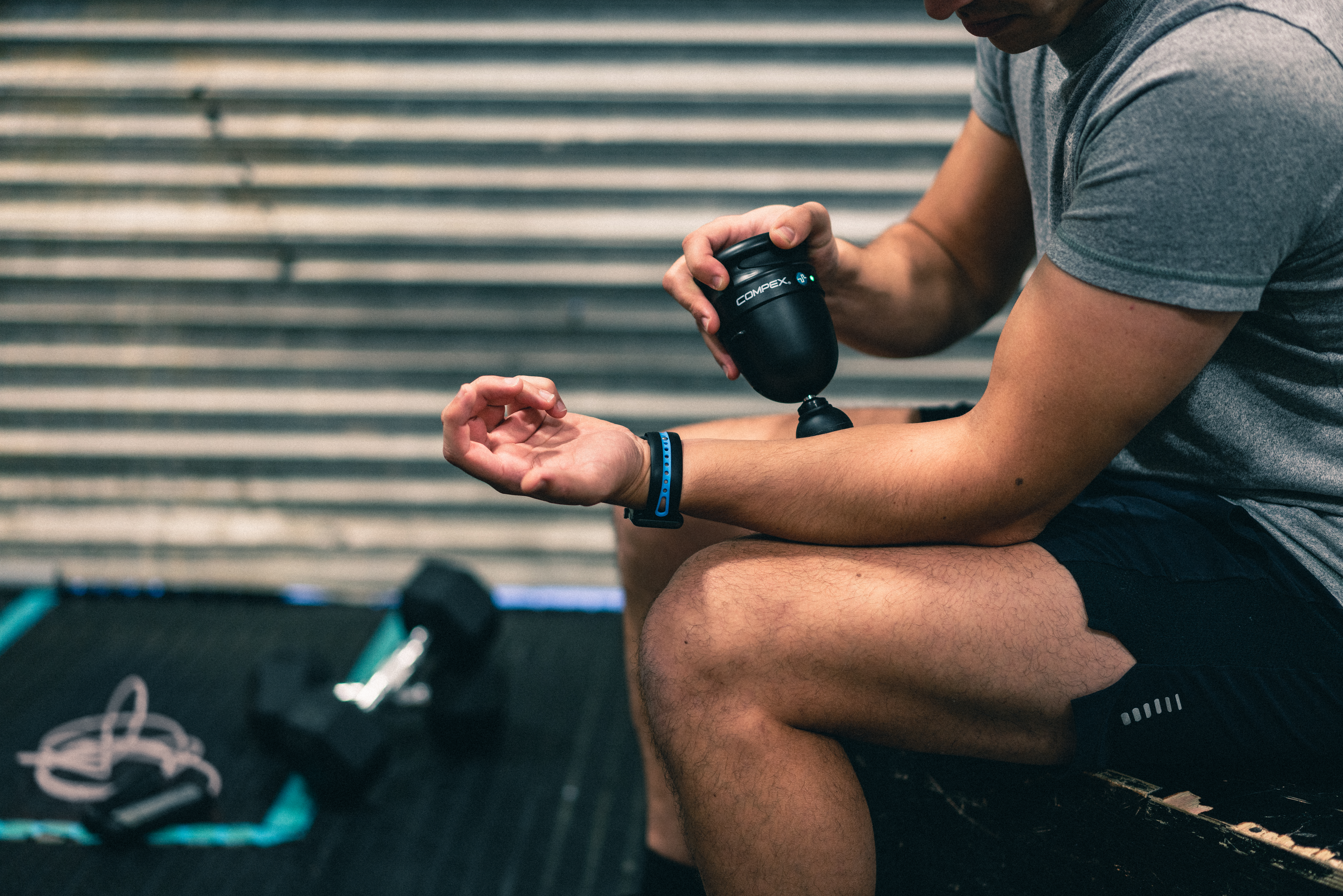 Person benutzt Compex Massagepistole am Arm im Fitnessstudio.
