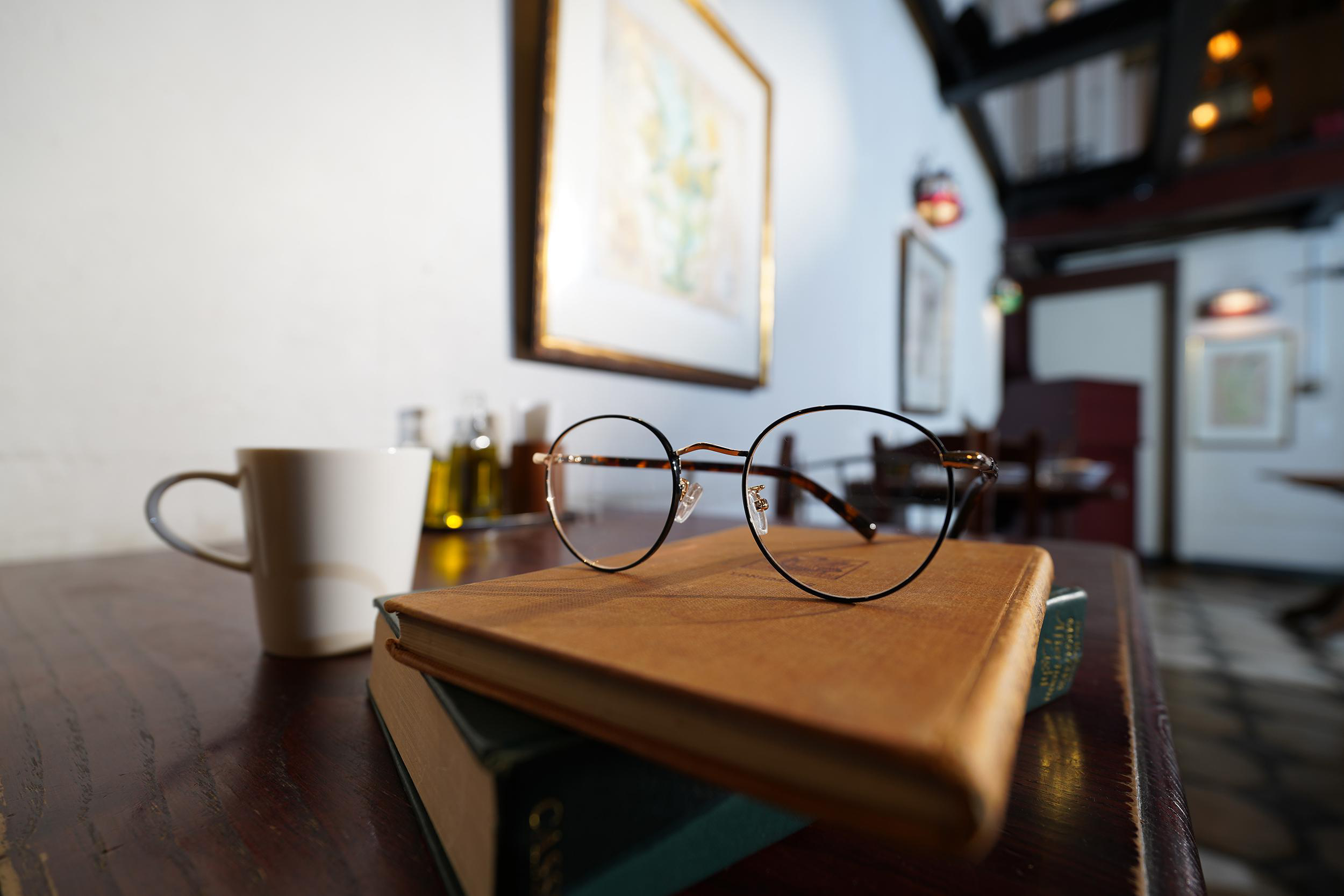 Brille auf einem Buch, mit einer Kaffeetasse und Hintergrund.