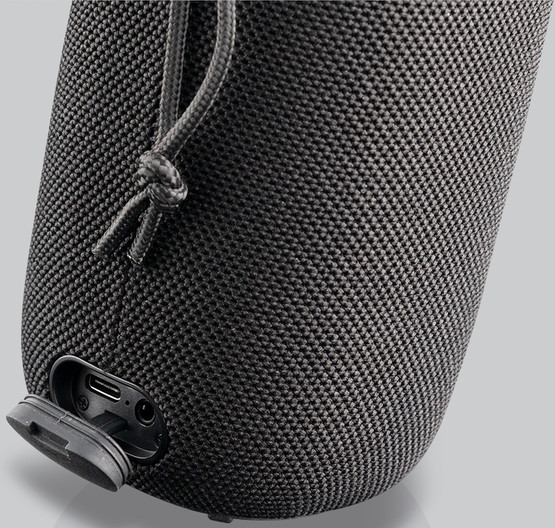 Un haut-parleur noir avec une texture en maille. Ports USB et de chargement visibles.