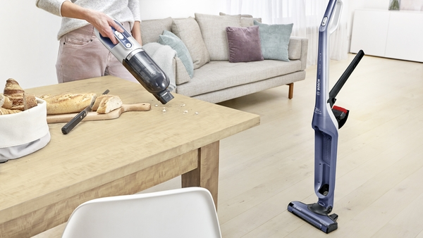 Person cleaning table with cordless vacuum. Bread and accessories are nearby.