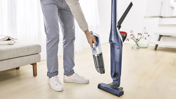 A person taking apart a blue and white cordless vacuum cleaner, showing the handheld component.
