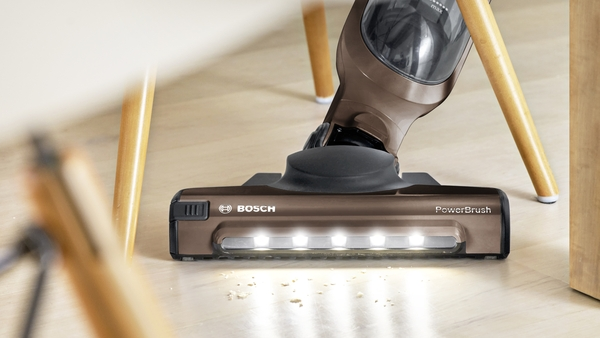A brown and black Bosch PowerBrush vacuum cleaner head on a wooden floor, with lights on.