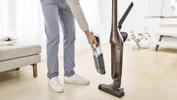 A man assembling a brown and white vacuum cleaner. Wooden floor and sunlight visible.
