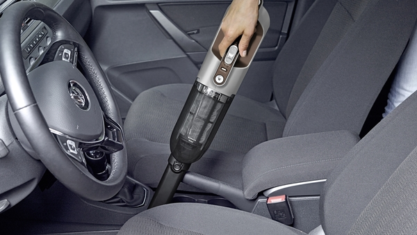 Hand using a vacuum cleaner in a car. The vacuum is being used on a car seat.