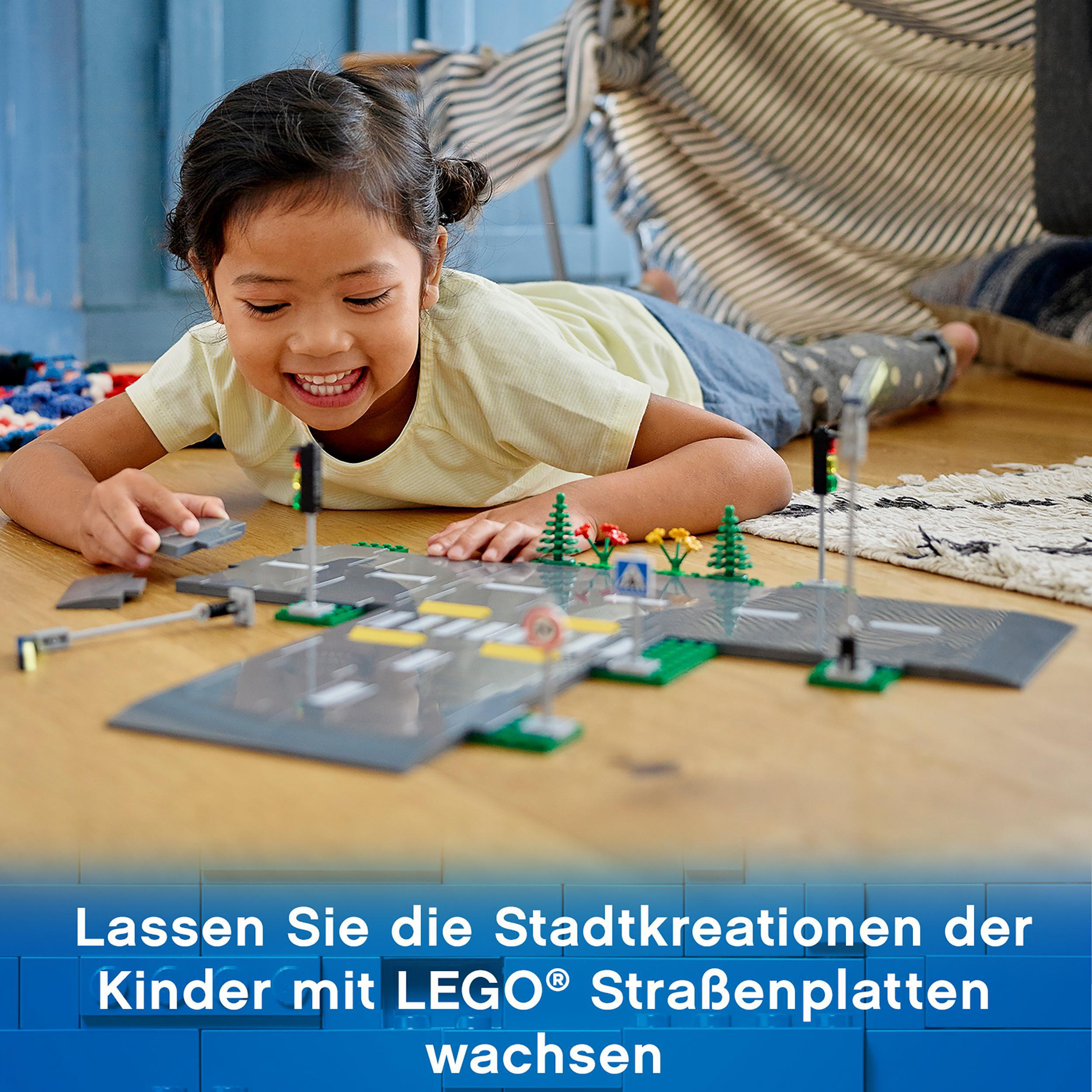 Ein junges Mädchen lächelt und spielt mit LEGO-Straßenplatten, Bäumen und Ampeln.