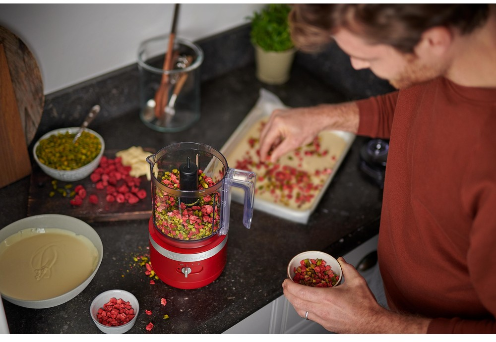 Een man in een rood shirt bereidt eten met een keukenmachine en ingrediënten.