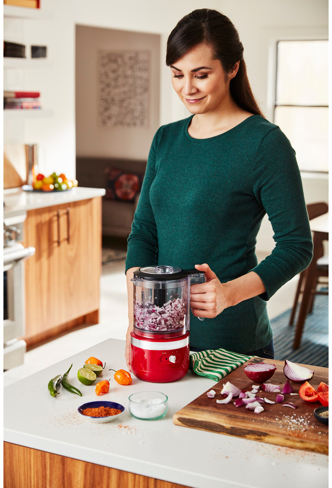 Vrouw houdt een rood keukenapparaat vast. Verschillende ingrediënten liggen op een aanrecht.