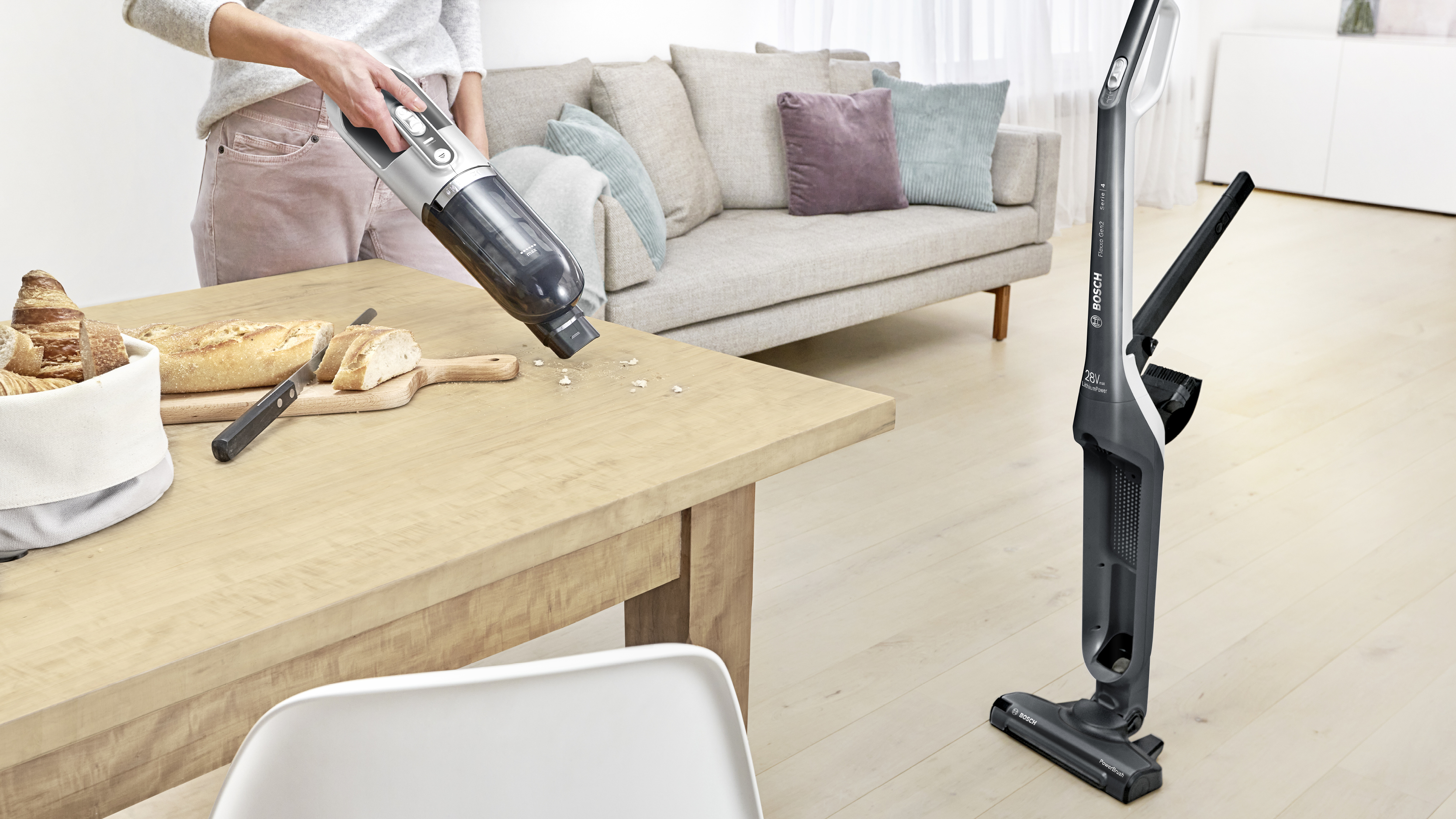Eine Frau, die einen Holztisch mit einem Bosch-Staubsauger absaugt, mit Brot und einem Sofa im Hintergrund.