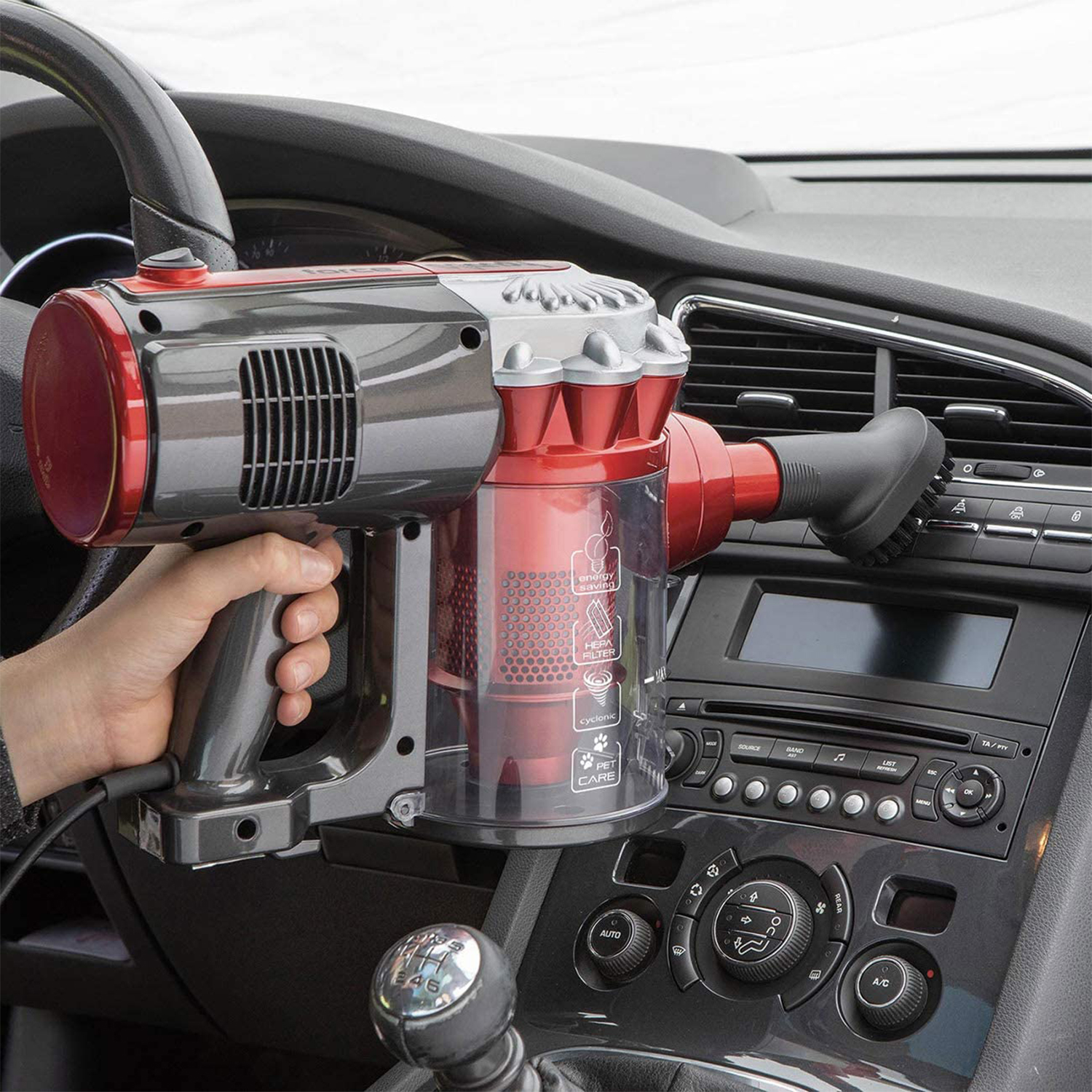 Un aspirapolvere portatile rosso e grigio viene tenuto all'interno di un'auto.