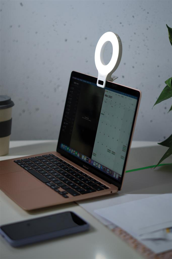 Laptop gyűrűfénnyel a tetején. Asztal jegyzettel, telefonnal és kávéscsészével. Világos háttér.