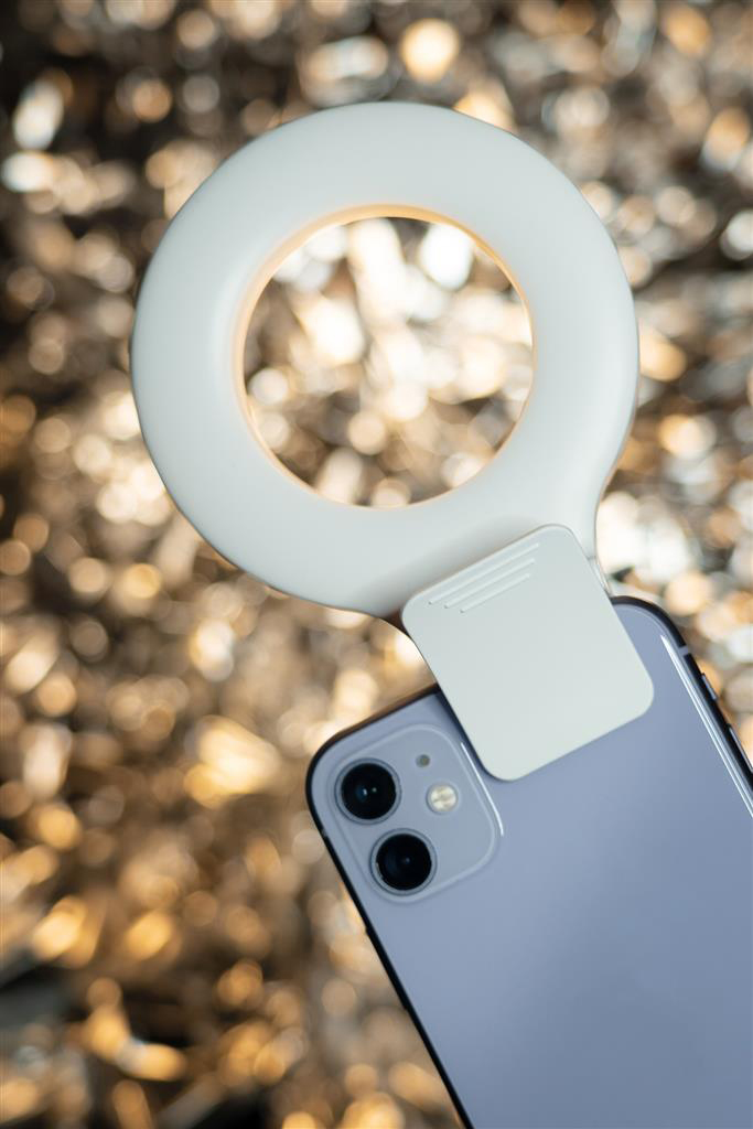Egy gyűrűs lámpa egy lila telefonhoz rögzítve. A háttér elmosódott bokeh effektus.