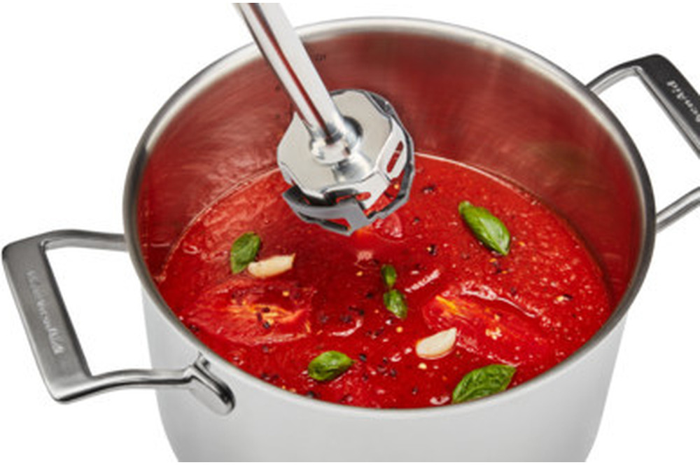 Un mixeur plongeant KitchenAid mélangeant une soupe de tomates dans une casserole.