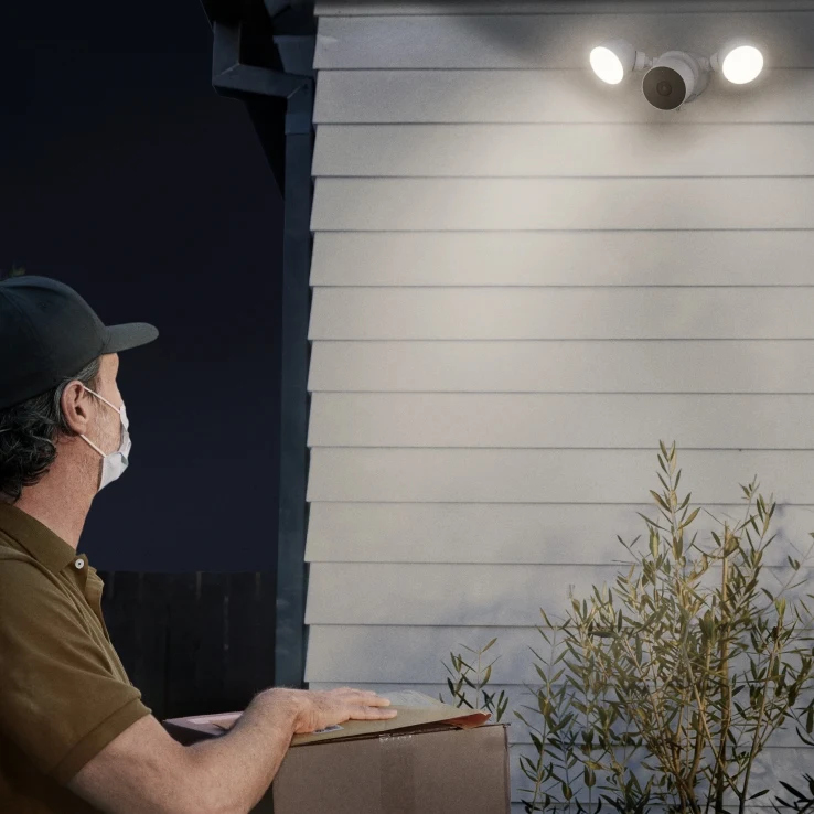 A person delivering a box at night. A house with a security light is in the background.
