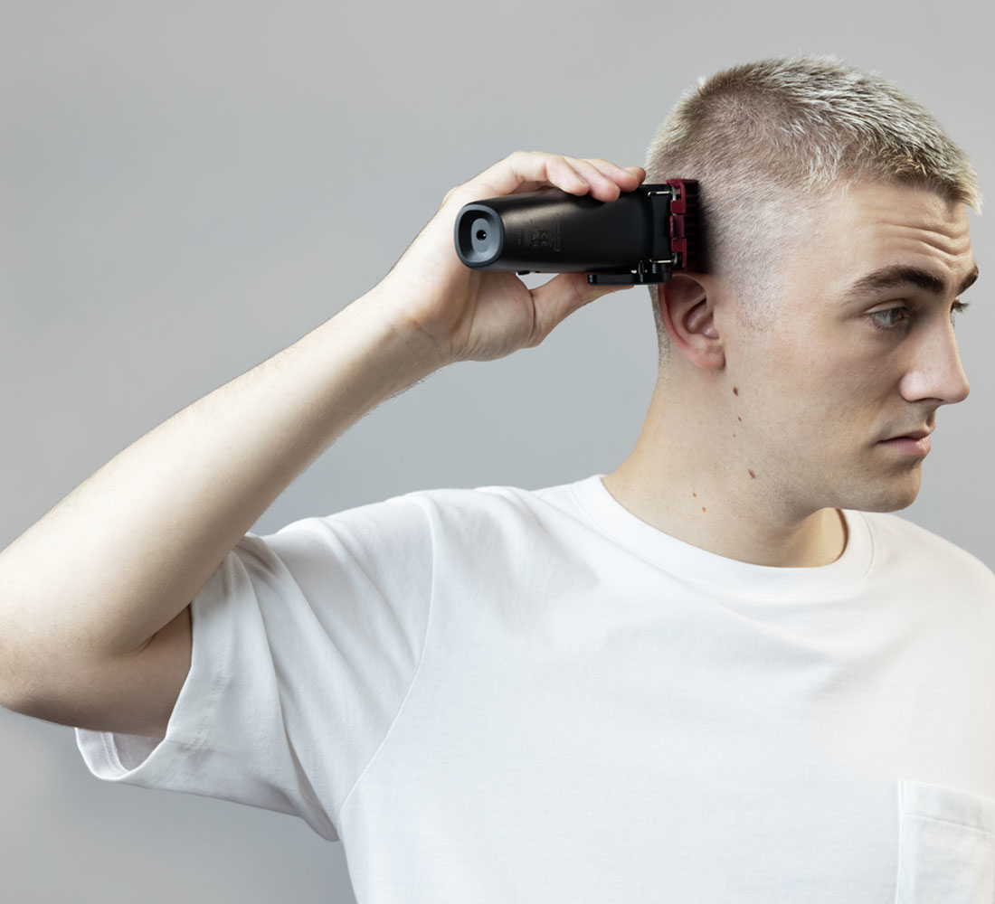 Een man knipt zijn haar met een zwarte tondeuse. Hij houdt hem tegen zijn hoofd.