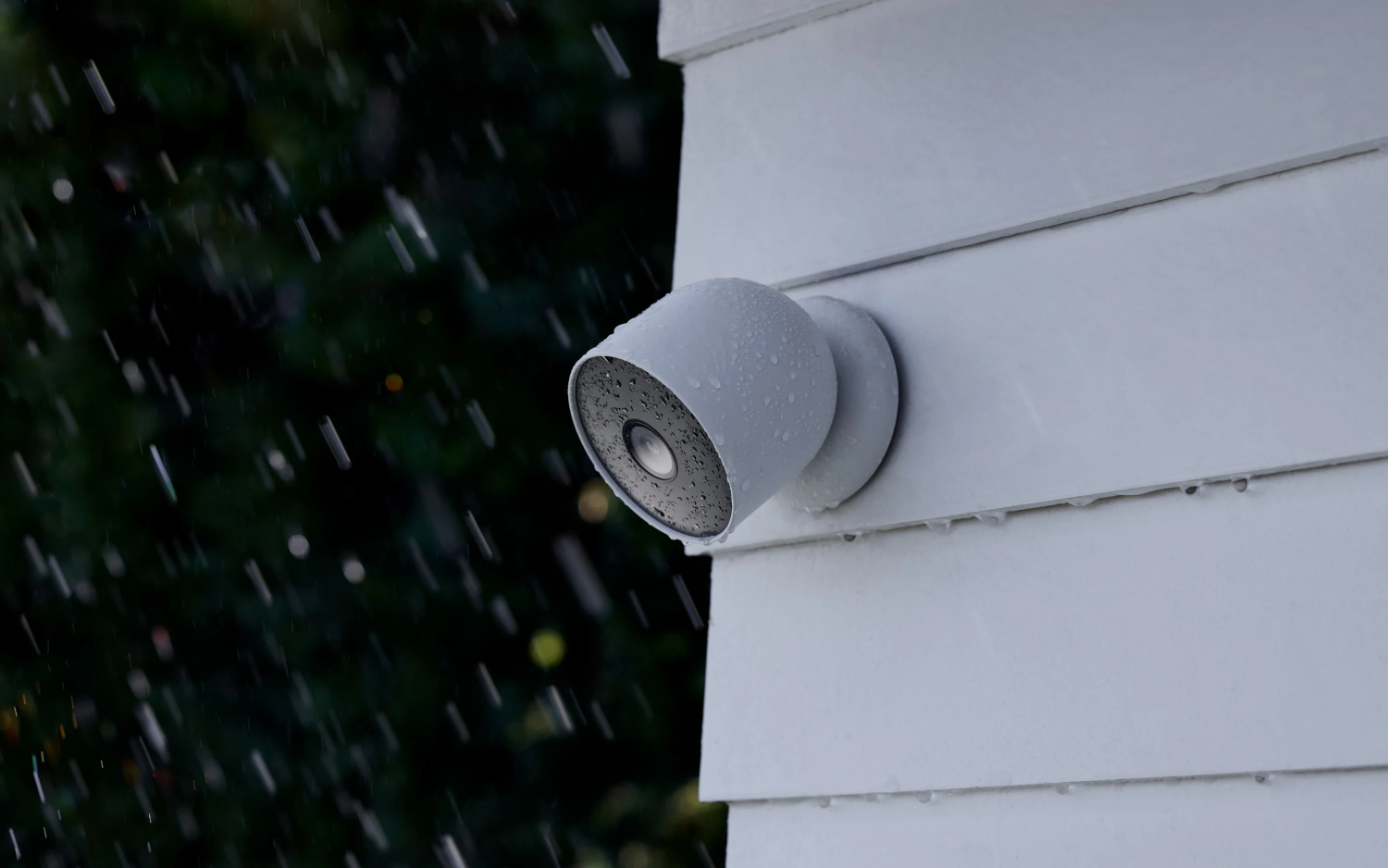 Een grijze beveiligingscamera gemonteerd op een wit huis, met regen ervoor.
