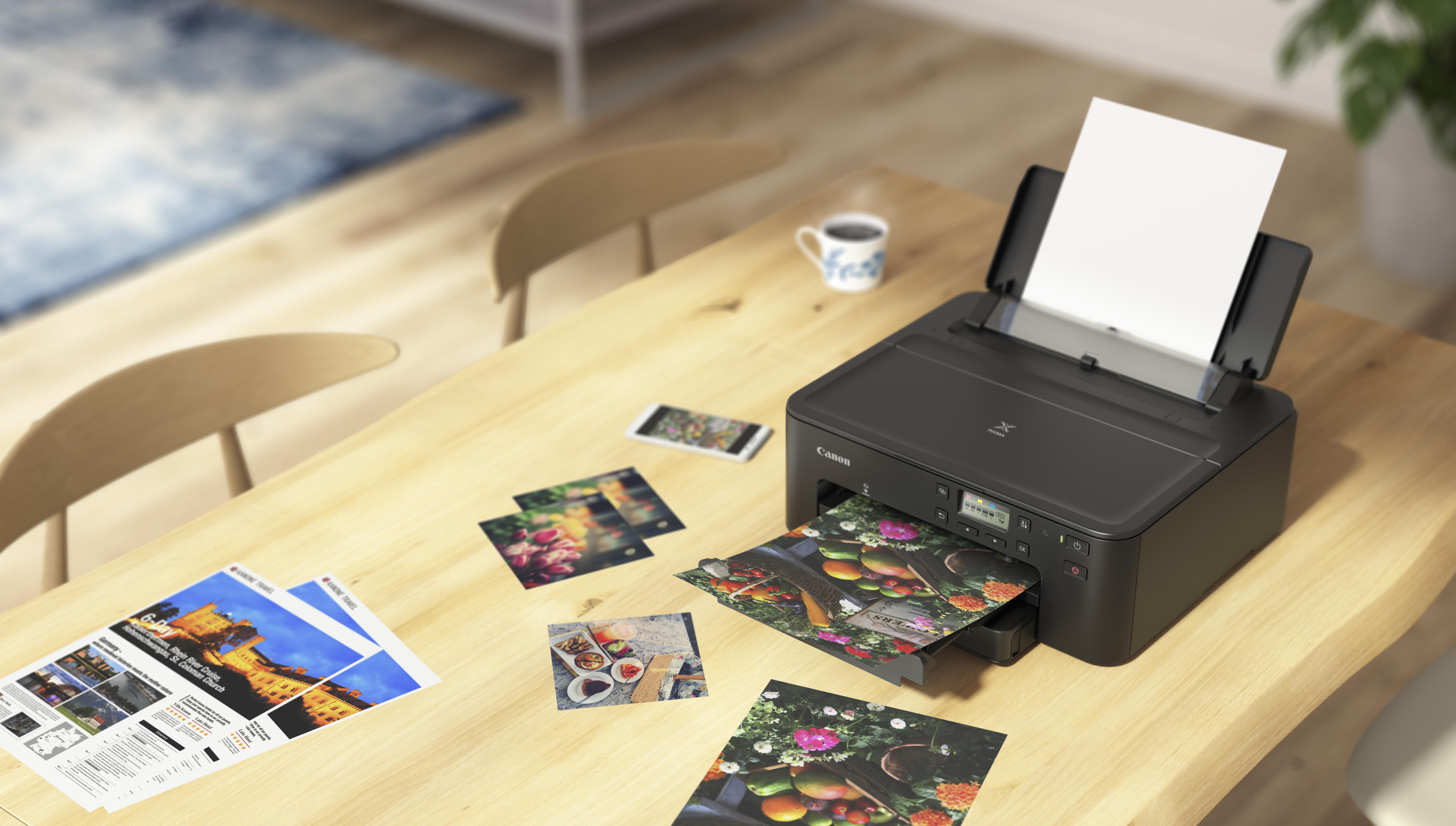 Ein Drucker druckt Farbfotos auf einem Holztisch. Andere gedruckte Fotos und Dokumente umgeben ihn.