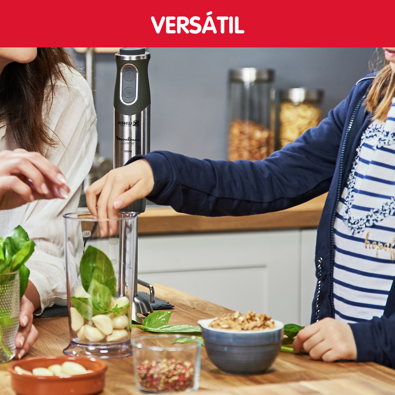 Dos personas preparando comida con una batidora. Los ingredientes incluyen albahaca, ajo y nueces. Titular rojo 'Versátil'.