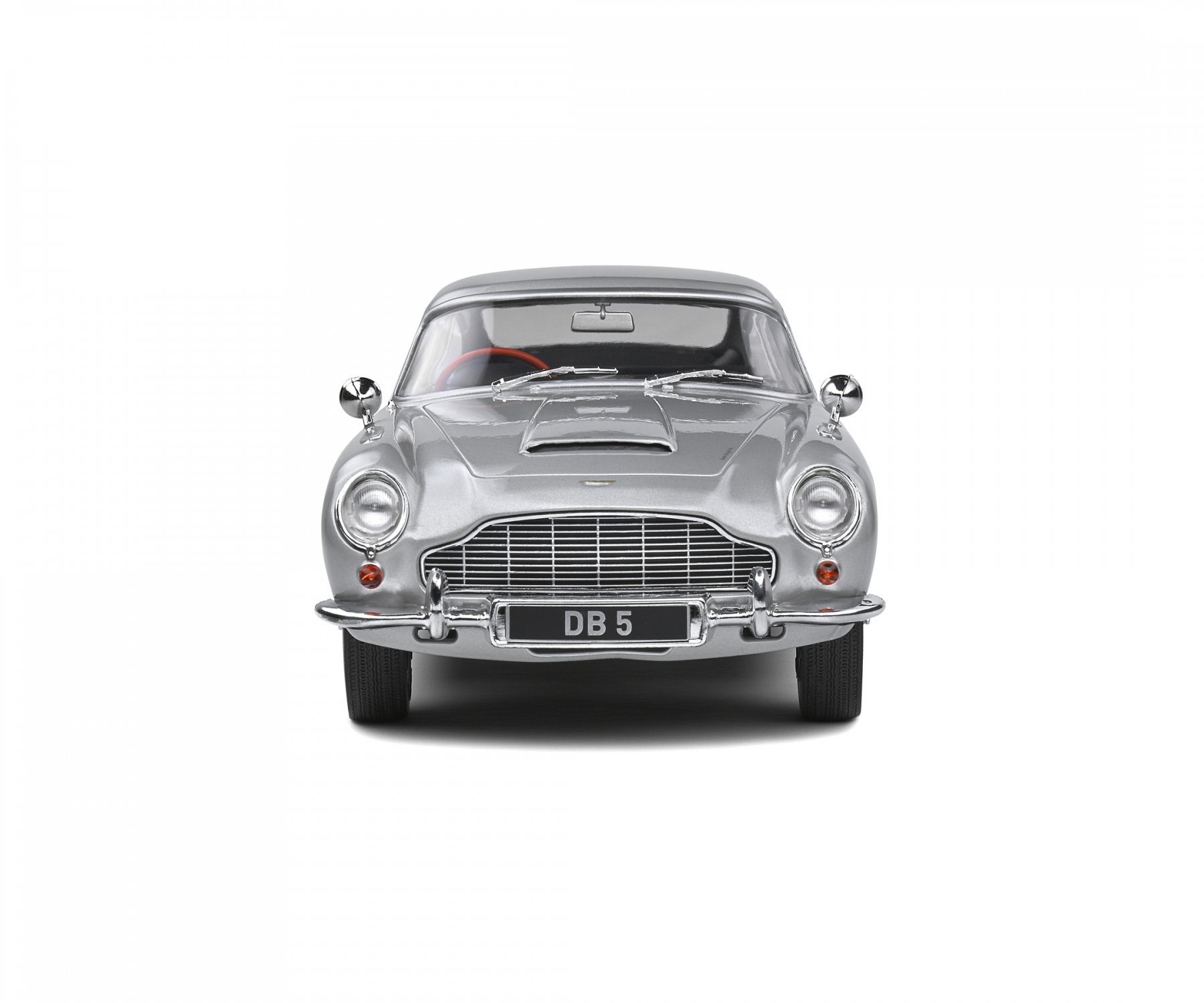 Ein silberner Aston Martin DB5 steht im Zentrum und blickt den Betrachter an. Das Auto hat ein Nummernschild mit der Aufschrift DB 5, vor weißem Hintergrund.