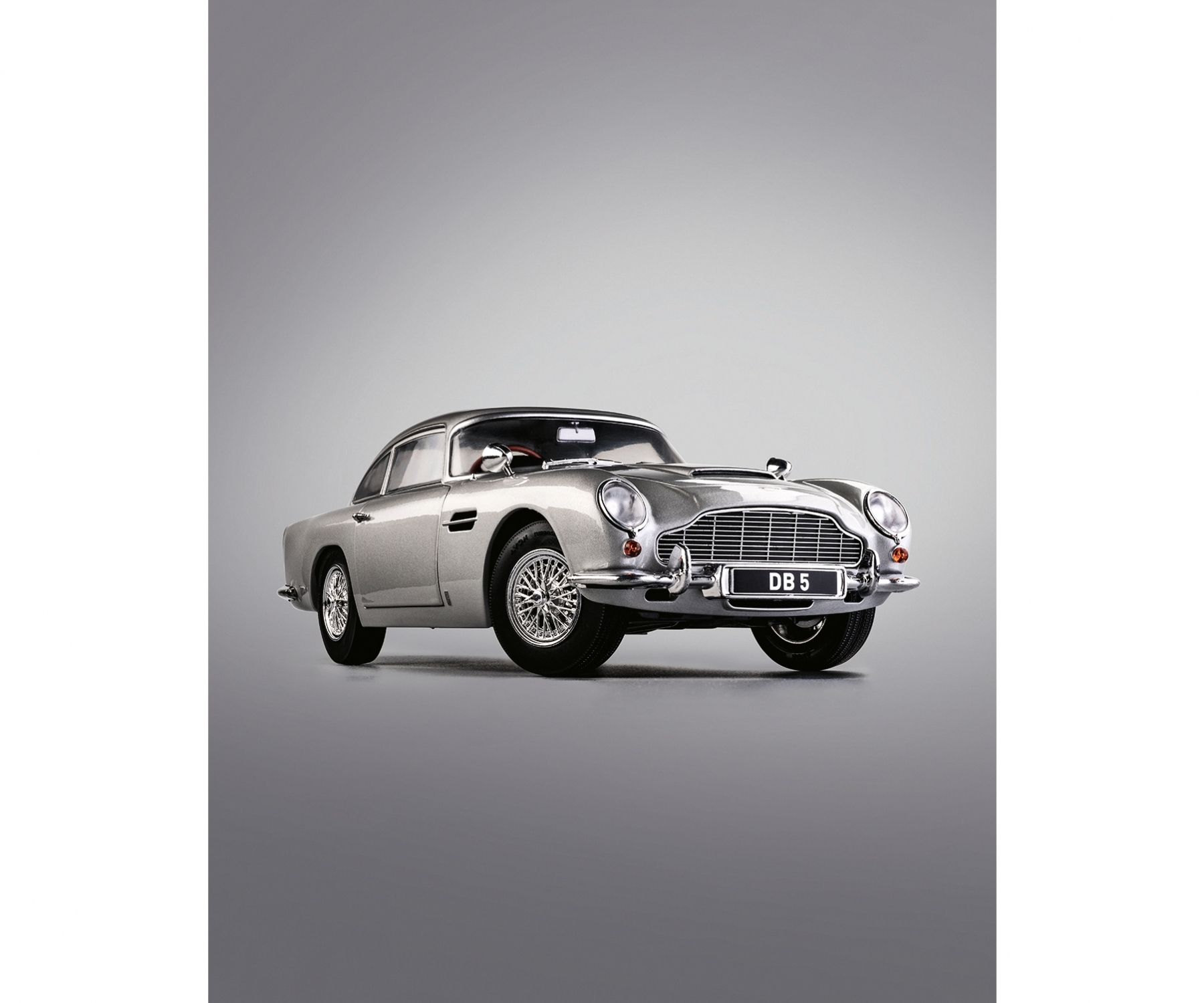 Silberner Aston Martin DB5 mit dem Kennzeichen DB 5 auf grauem Hintergrund. Das Auto ist in perfektem Zustand.