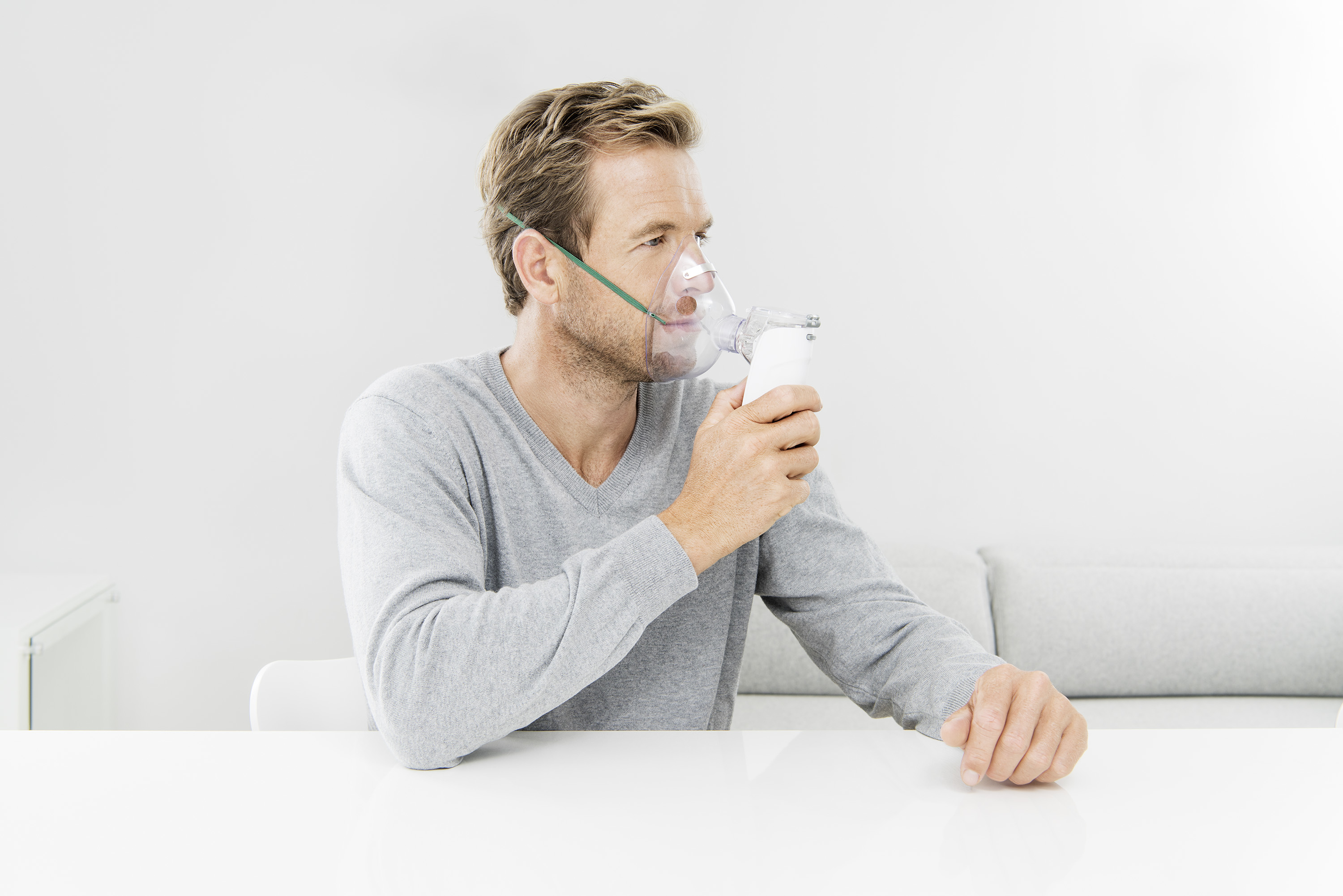 Ein Mann mit einer Sauerstoffmaske, der an einem weißen Tisch sitzt.