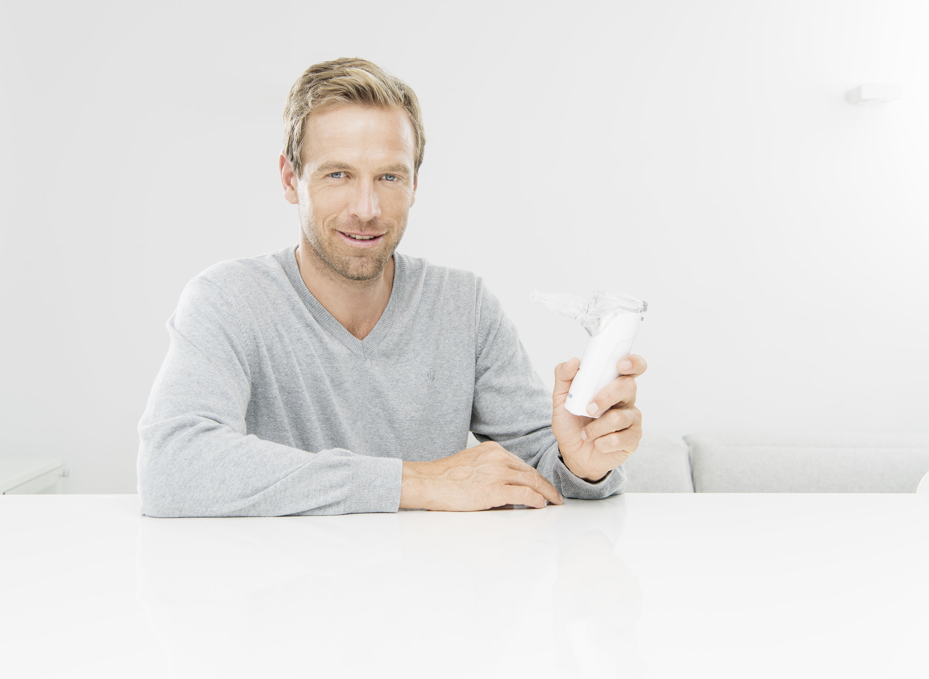 Mann sitzt, hält einen weißen Vernebler, lächelt den Betrachter an. Weißer Hintergrund.