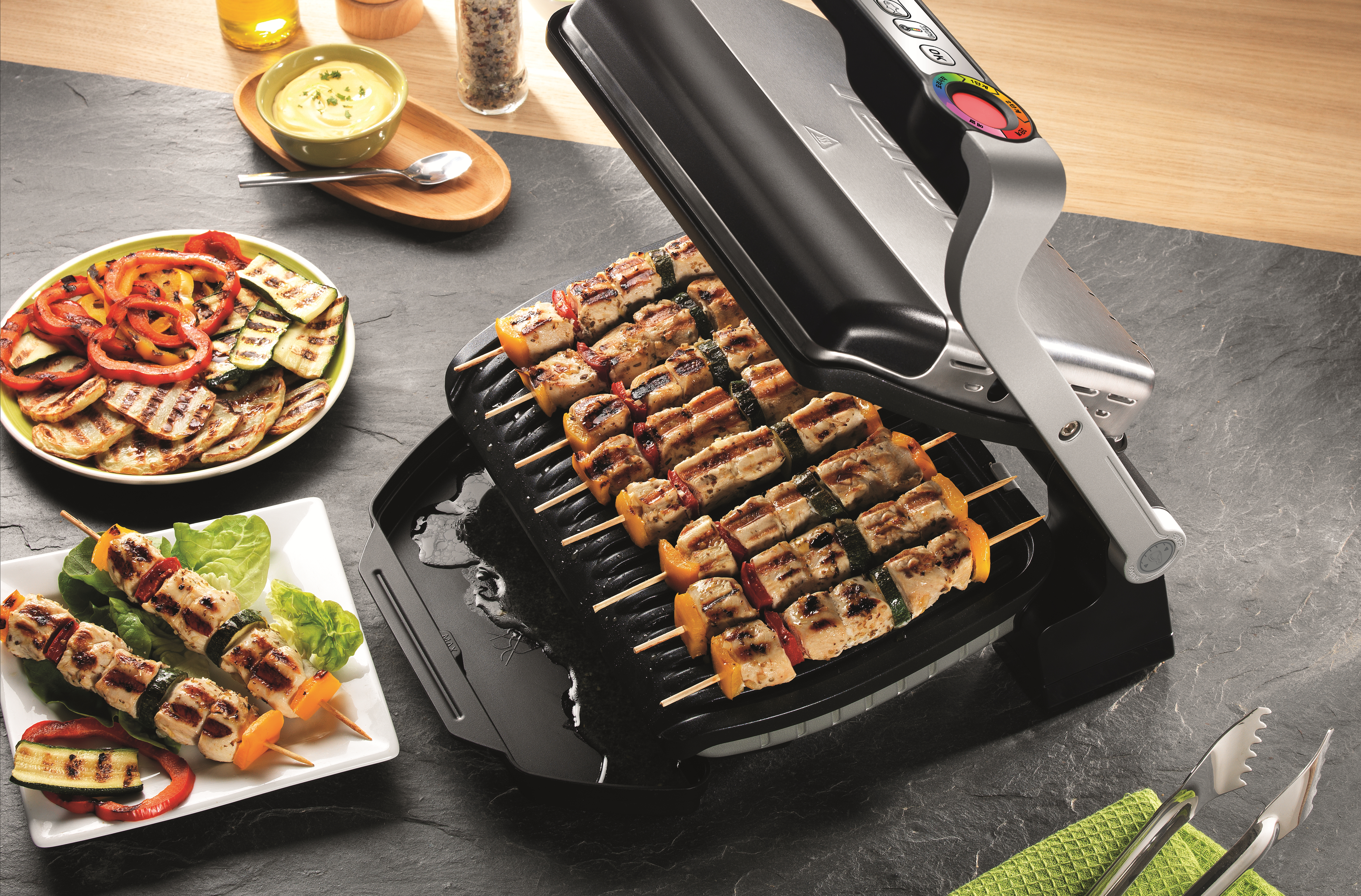 Ein Grill mit gegrilltem Essen. Spieße mit Hähnchen und Gemüse, gegrillte Paprika und eine Soße sind vorhanden.
