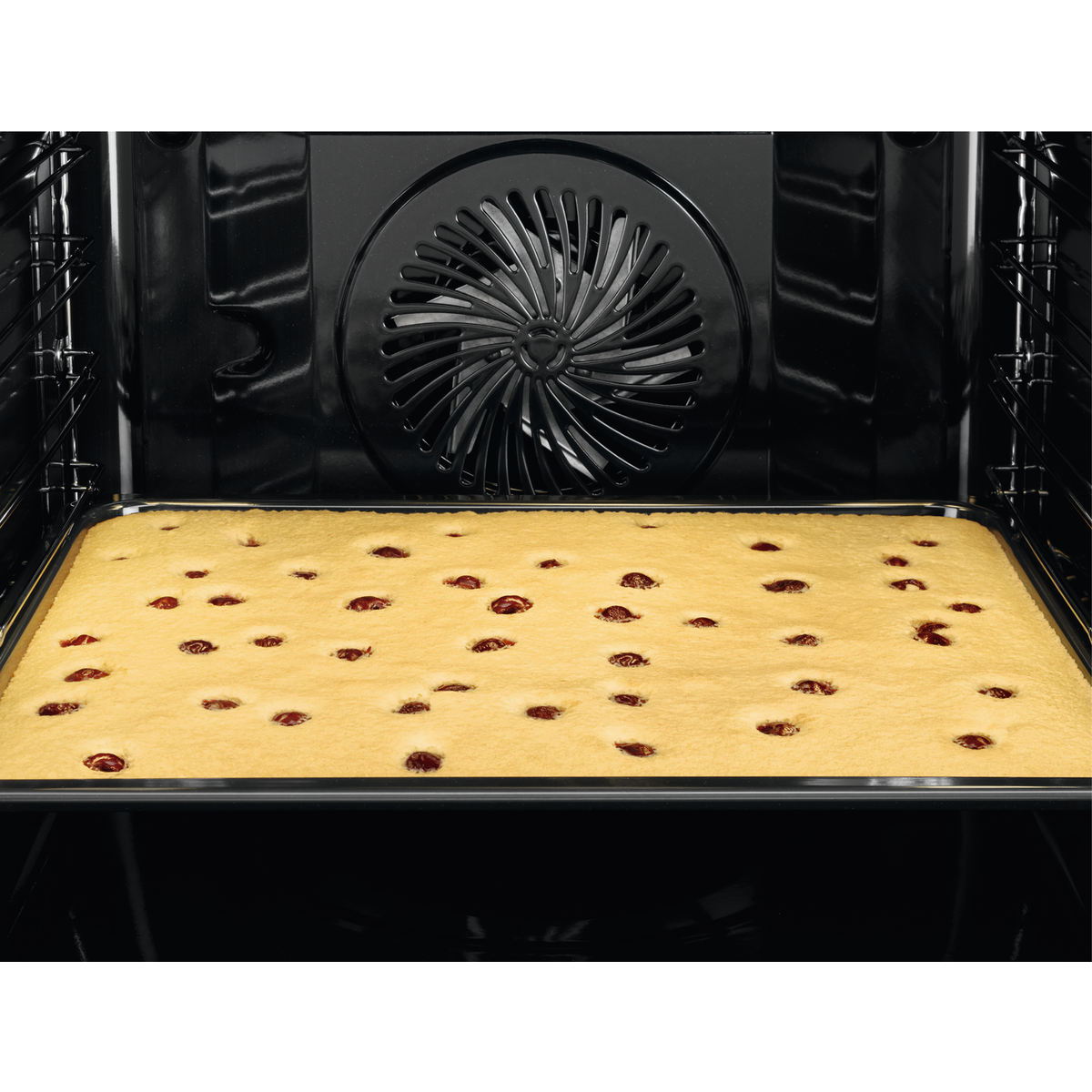 Een oveninterieur met een gebakken cake met kersen.