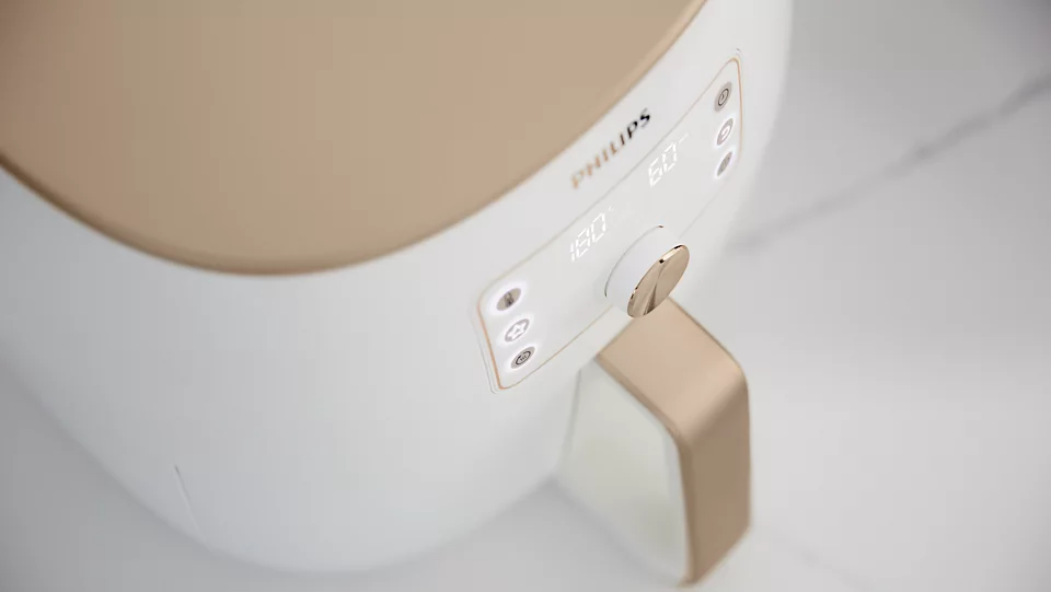 Fehér és arany légkeveréses sütő digitális kijelzővel. 180 fokot és 60 percet mutat. Philips márkanév látható.