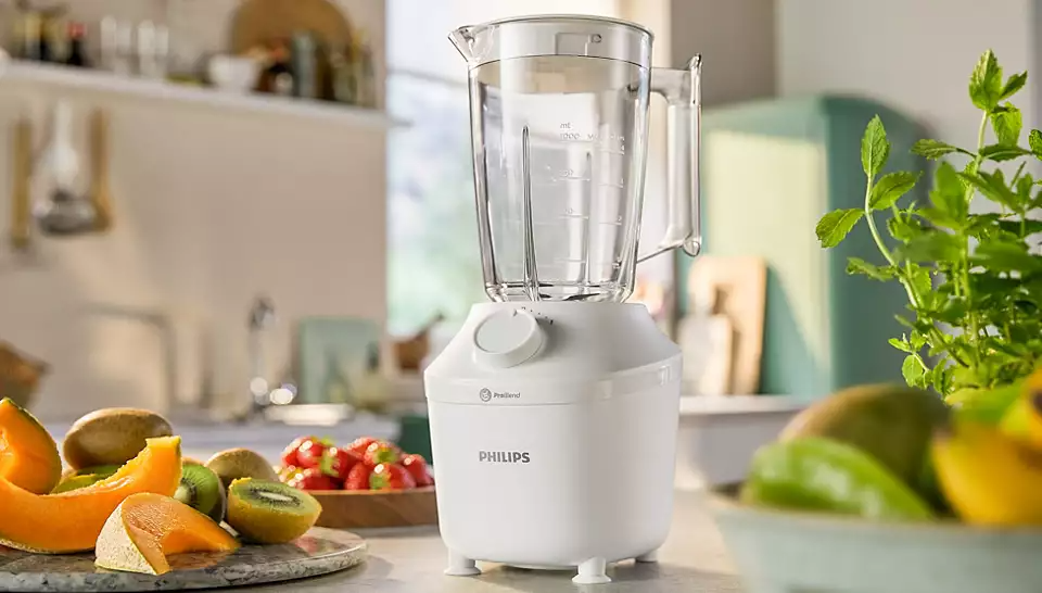 Fehér Philips turmixgép. Egy pulton van gyümölccsel. Konyhai háttér mentazöld szekrénnyel.