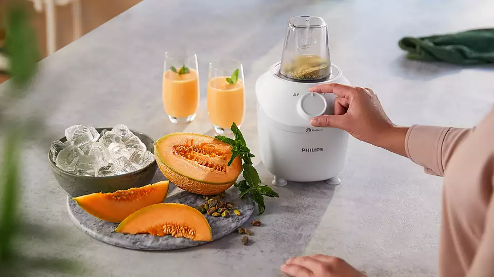 Egy nő Philips turmixgépet használ, hozzávalókkal, mint a sárgadinnye, menta és jégkockák.