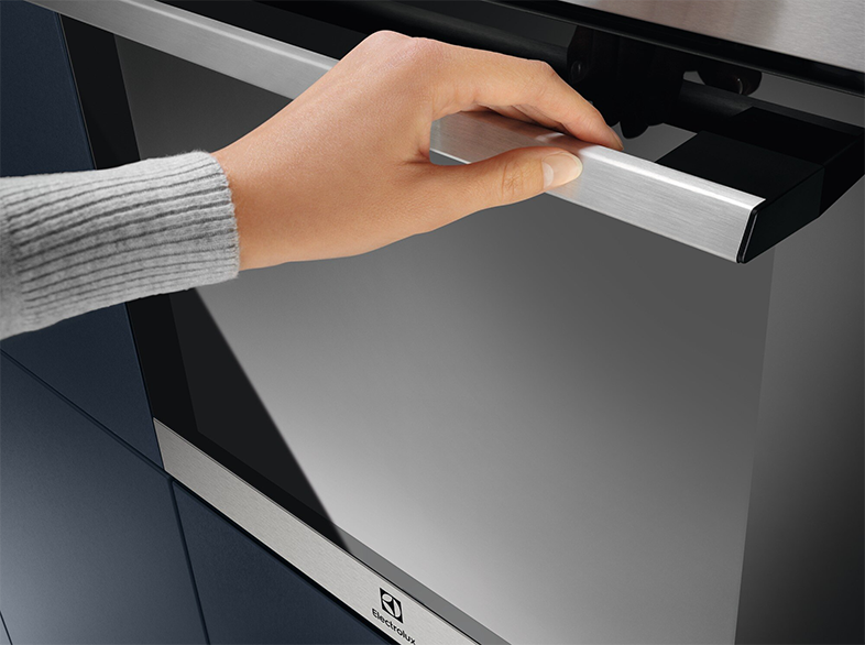 Kéz nyit egy rozsdamentes acél sütőajtót. A márka az Electrolux.