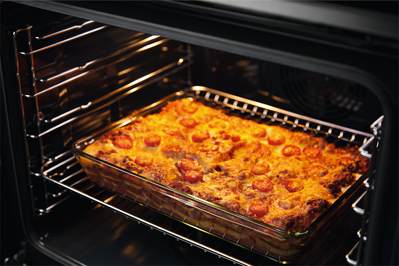 Lasagne egy üvegtálban a sütőben. Paradicsom a tetején, aranybarna. A sütő belseje látható.