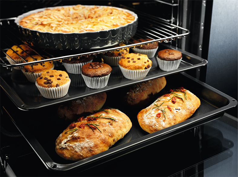 Egy sütőben tál, muffinok és kenyér található a rácsokon.