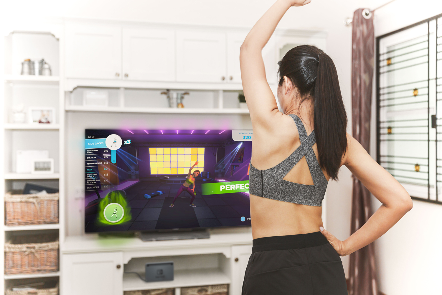 Eine Frau, die vor einem Fernseher trainiert, der ein Workout-Video zeigt, Arme erhoben.