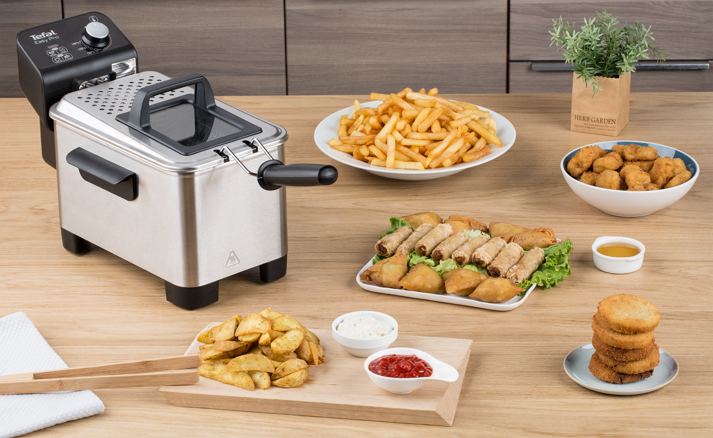 A stainless steel deep fryer with various fried foods on a wooden table.
