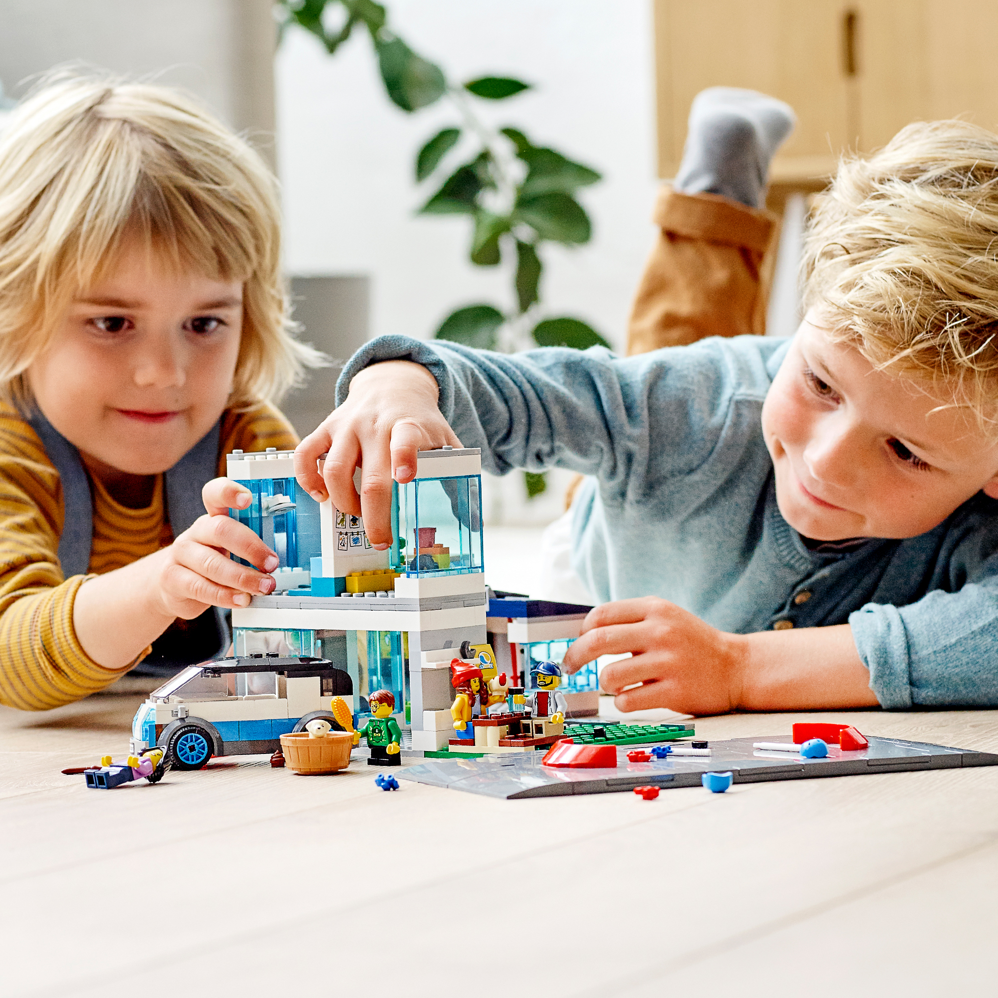 Zwei Kinder spielen mit einem Lego-Set eines Gebäudes, Autos und Figuren.