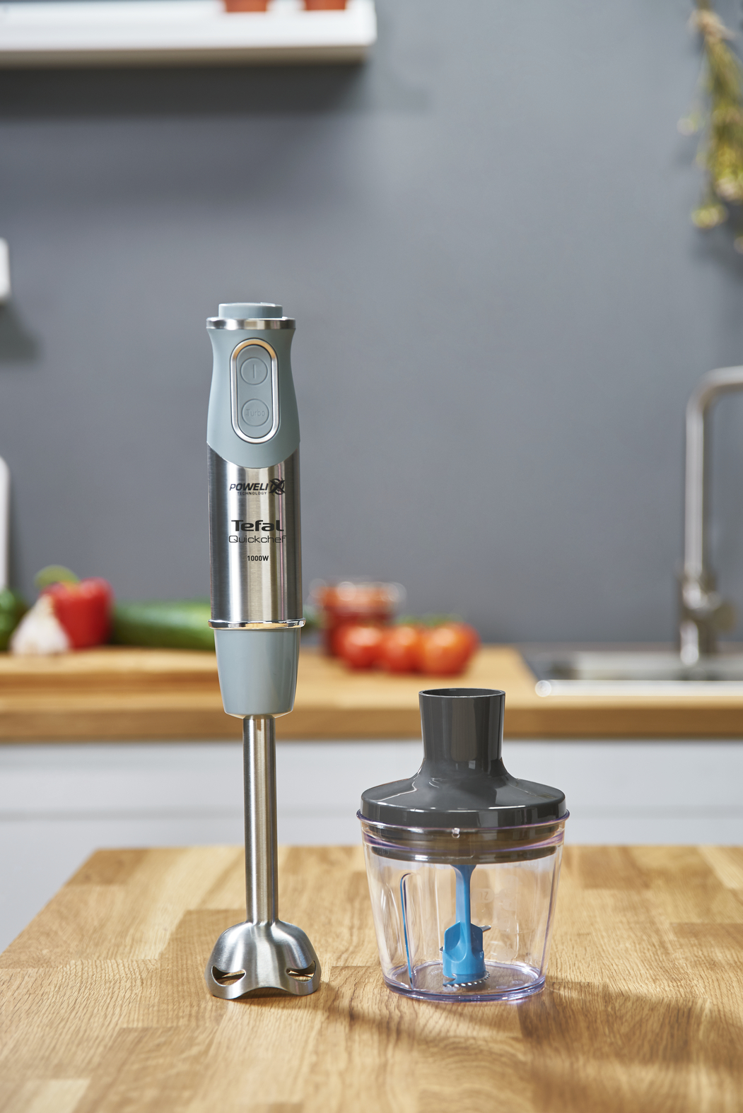 Blender en container op een houten oppervlak. Rode tomaten en andere items op het aanrecht.