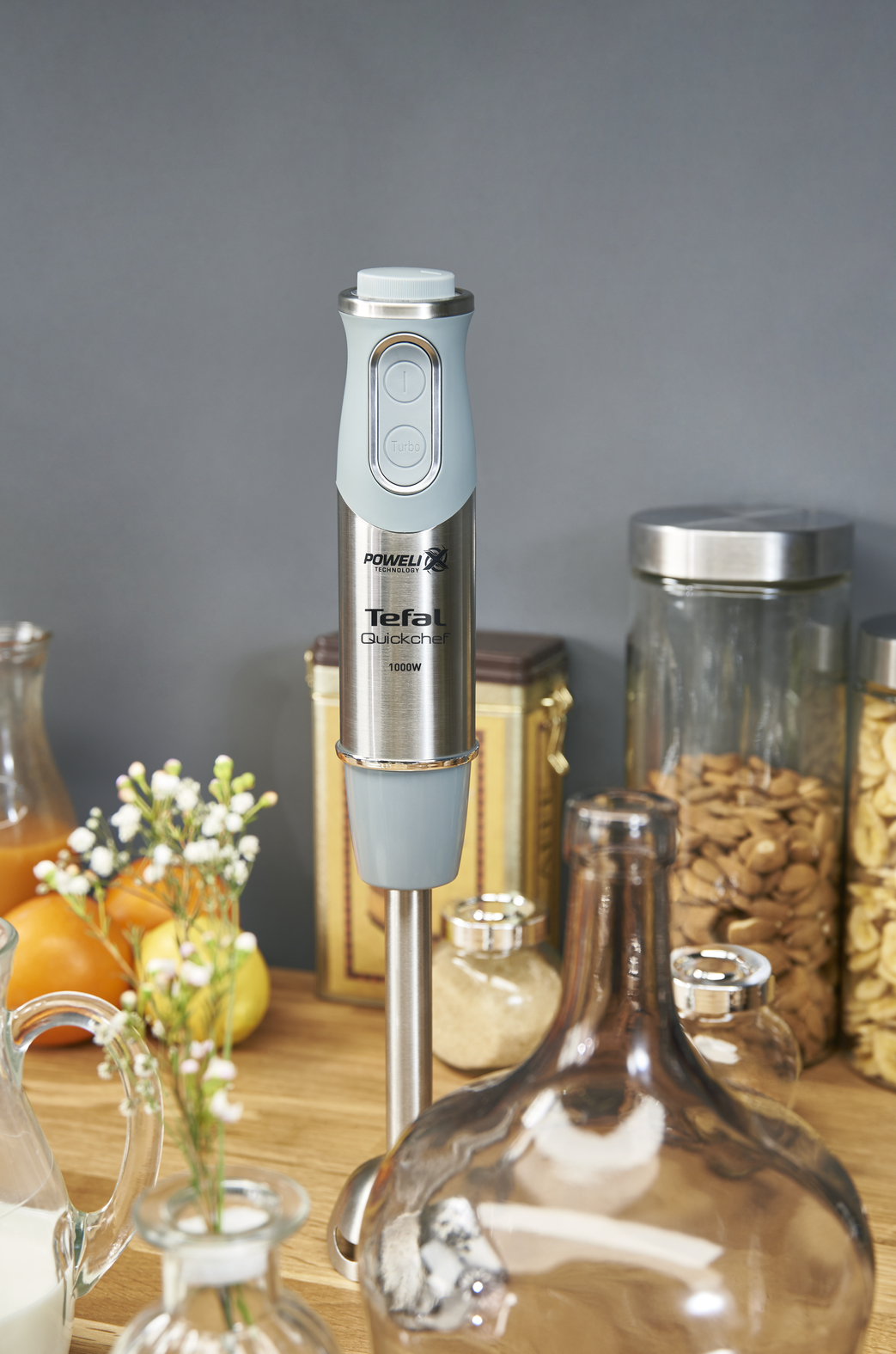 Tefal Quickchef staafmixer op een houten oppervlak met ingrediënten op de achtergrond.