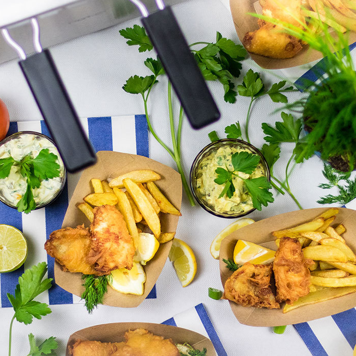 Vista dall'alto di pesce fritto e patatine fritte in barchette di carta con salse e guarnizioni.