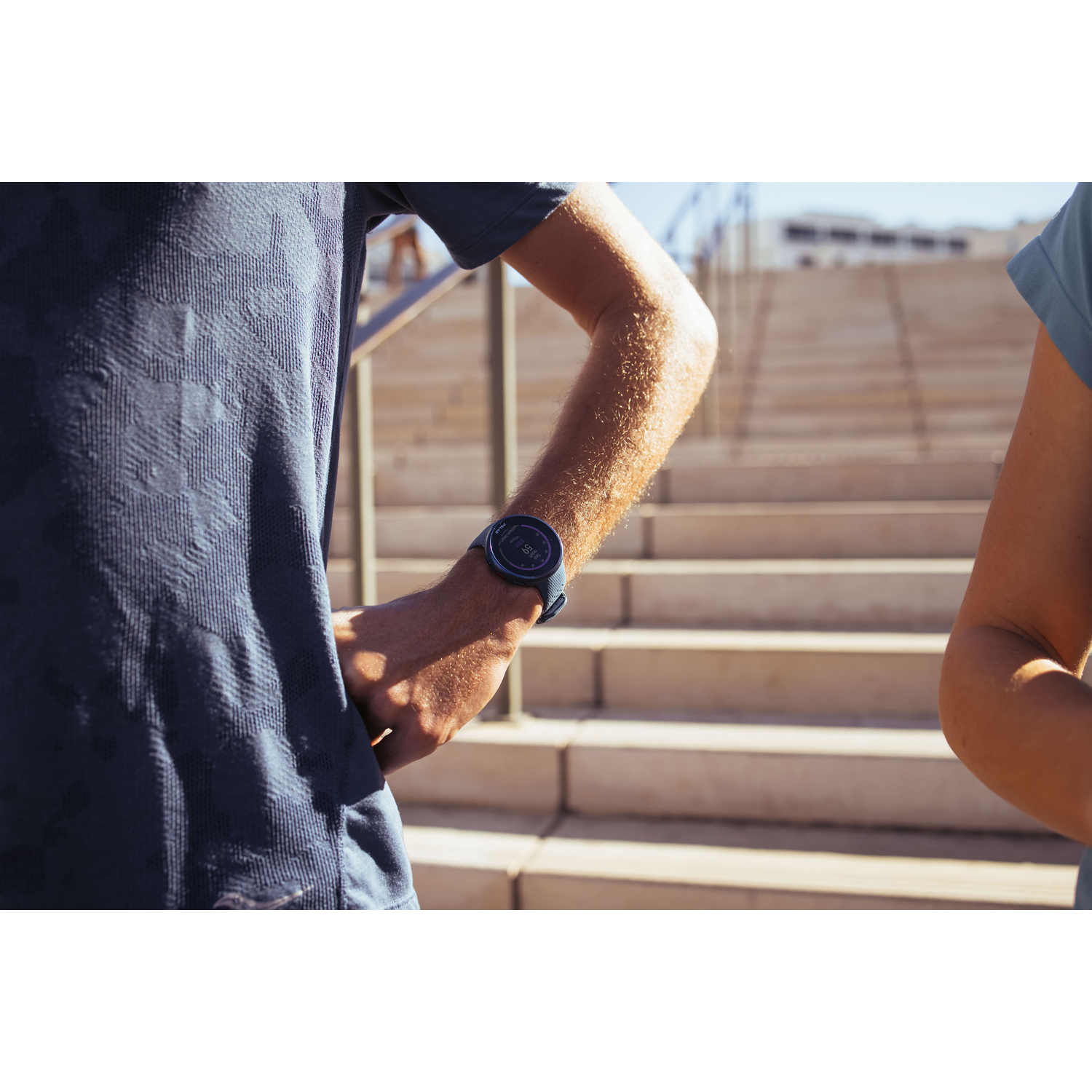 Dos personas en ropa casual junto a una escalera; una lleva reloj.